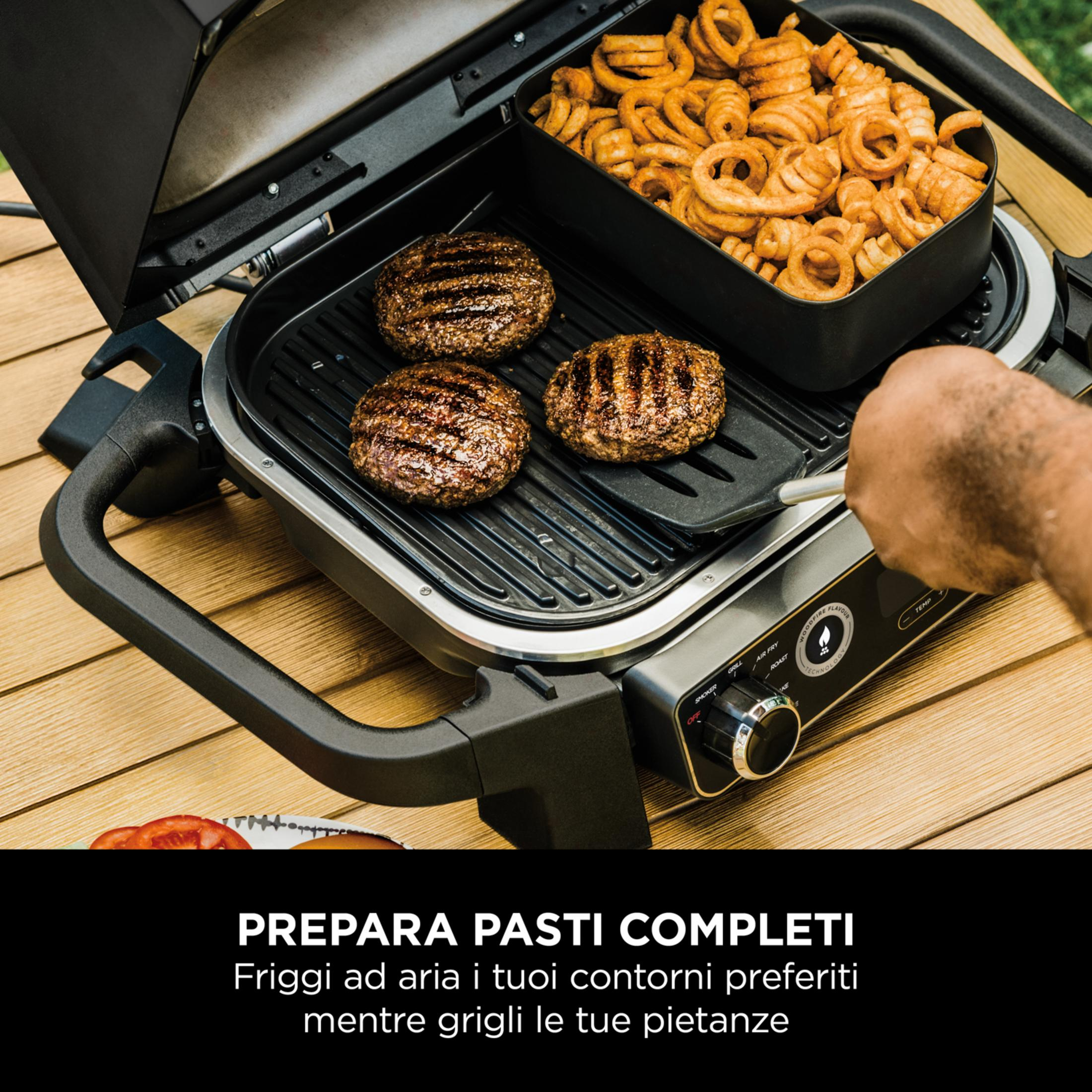 Burgerki i frytki na grillu z otwartą pokrywą. Ręka używa łopatki.