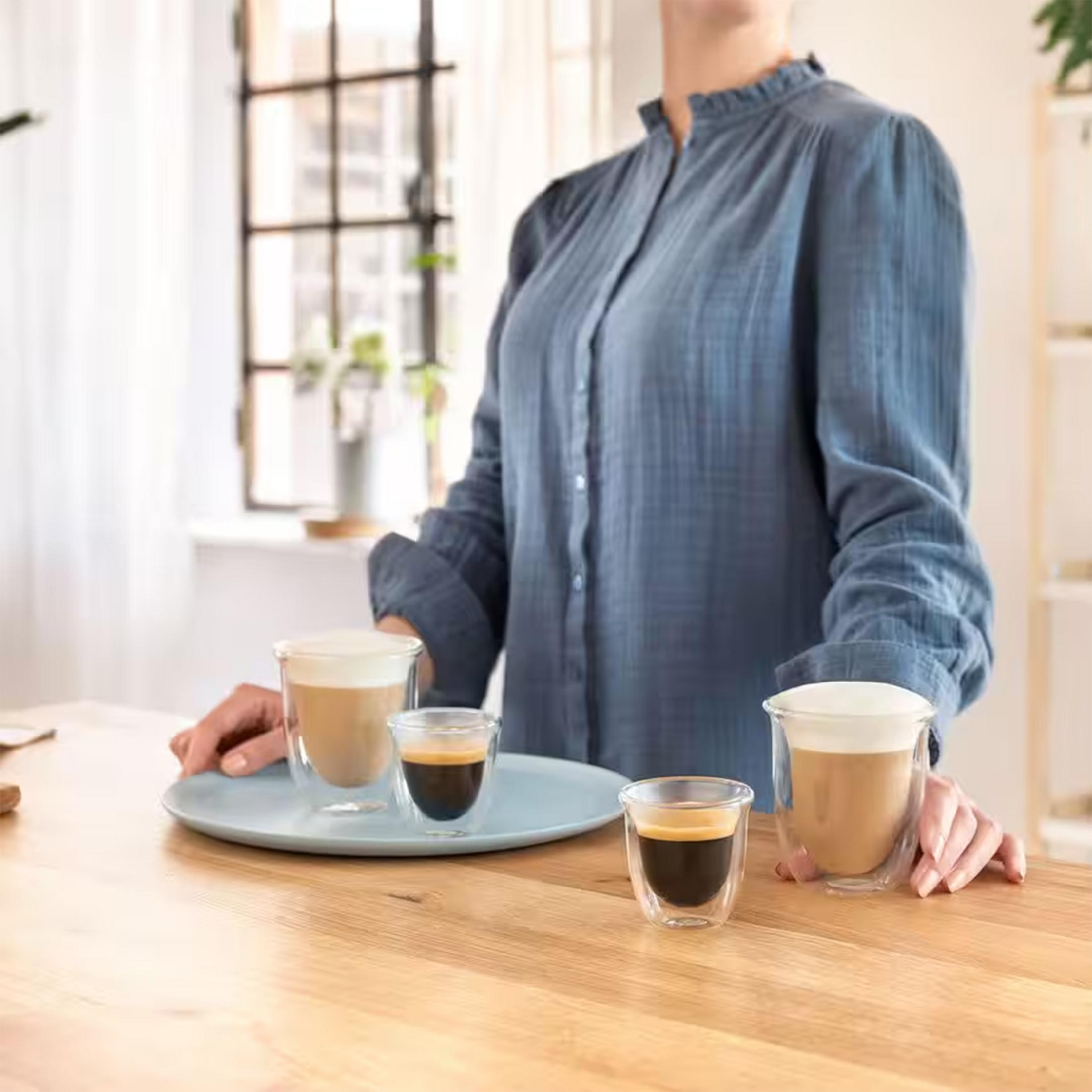 Eine Person in einem blauen Hemd serviert Kaffeegetränke in Glasbechern.