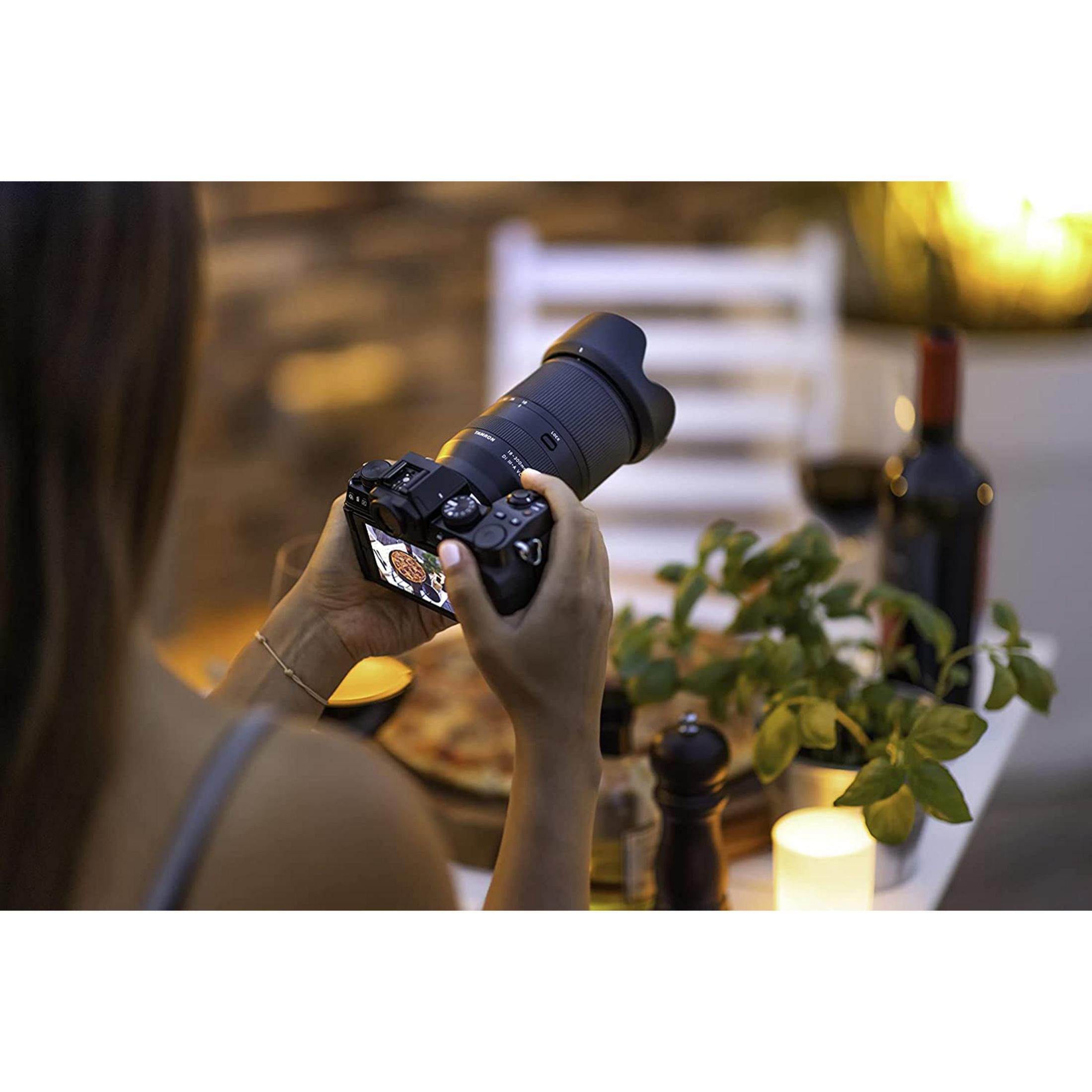 Osoba trzyma aparat z dużym obiektywem, fotografując pizzę przy stole.