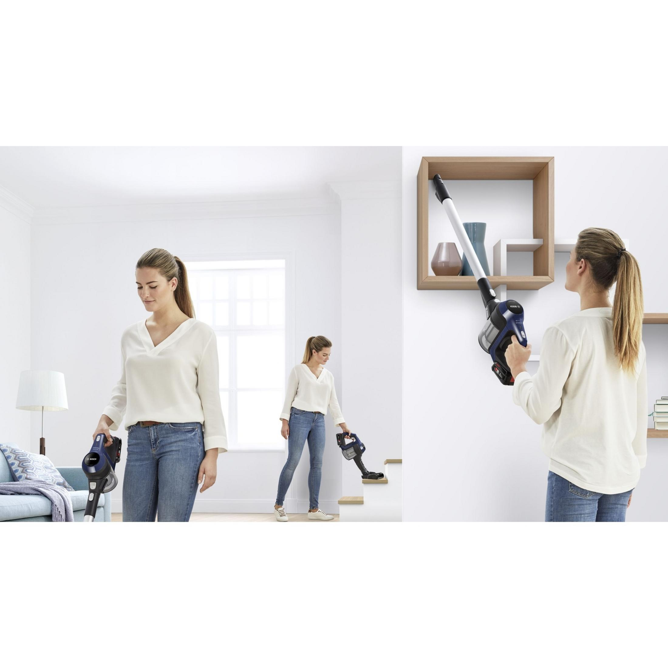 Una mujer aspira escaleras y estantes en una casa con una aspiradora inalámbrica azul.