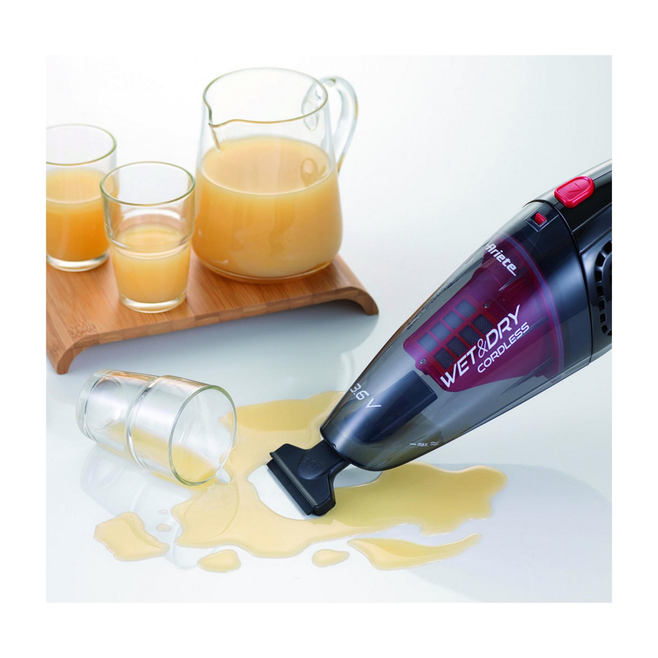 Ein Handstaubsauger saugt verschütteten Saft von einer weißen Oberfläche auf.