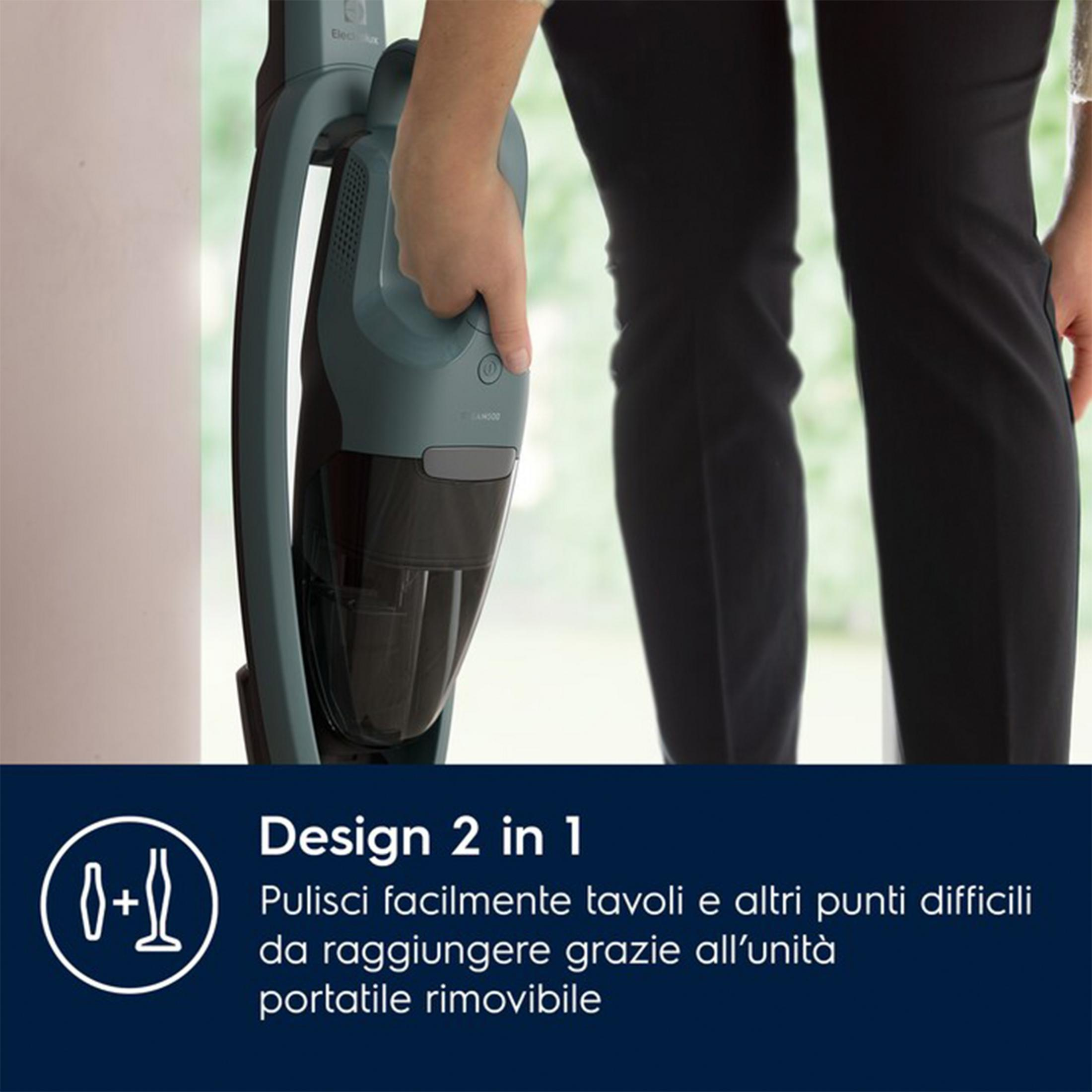 Una mano tiene un aspirapolvere grigio scuro davanti a pantaloni neri. Testo.