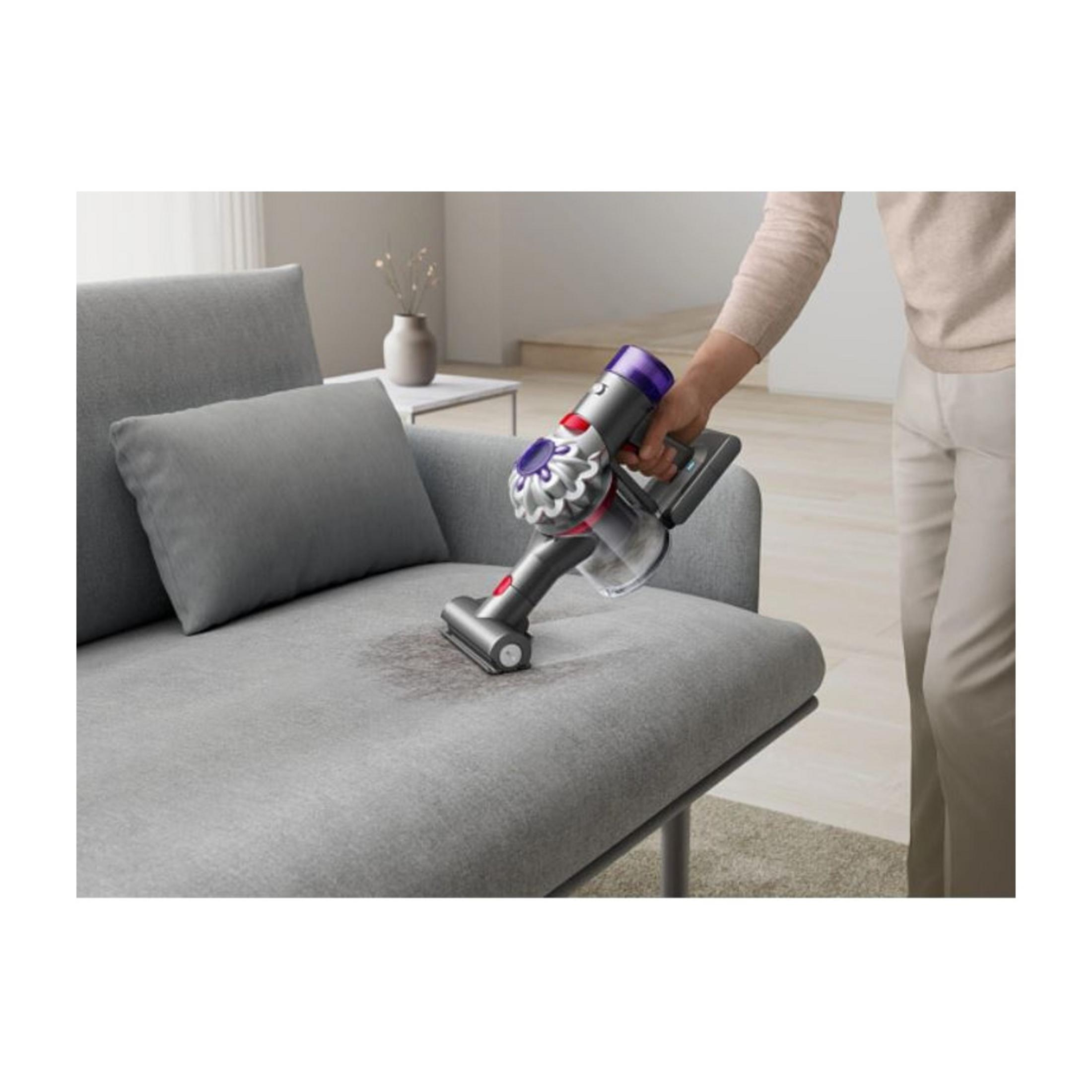 Eine Hand hält einen grauen Staubsauger, der auf einem grauen Sofa reinigt.
