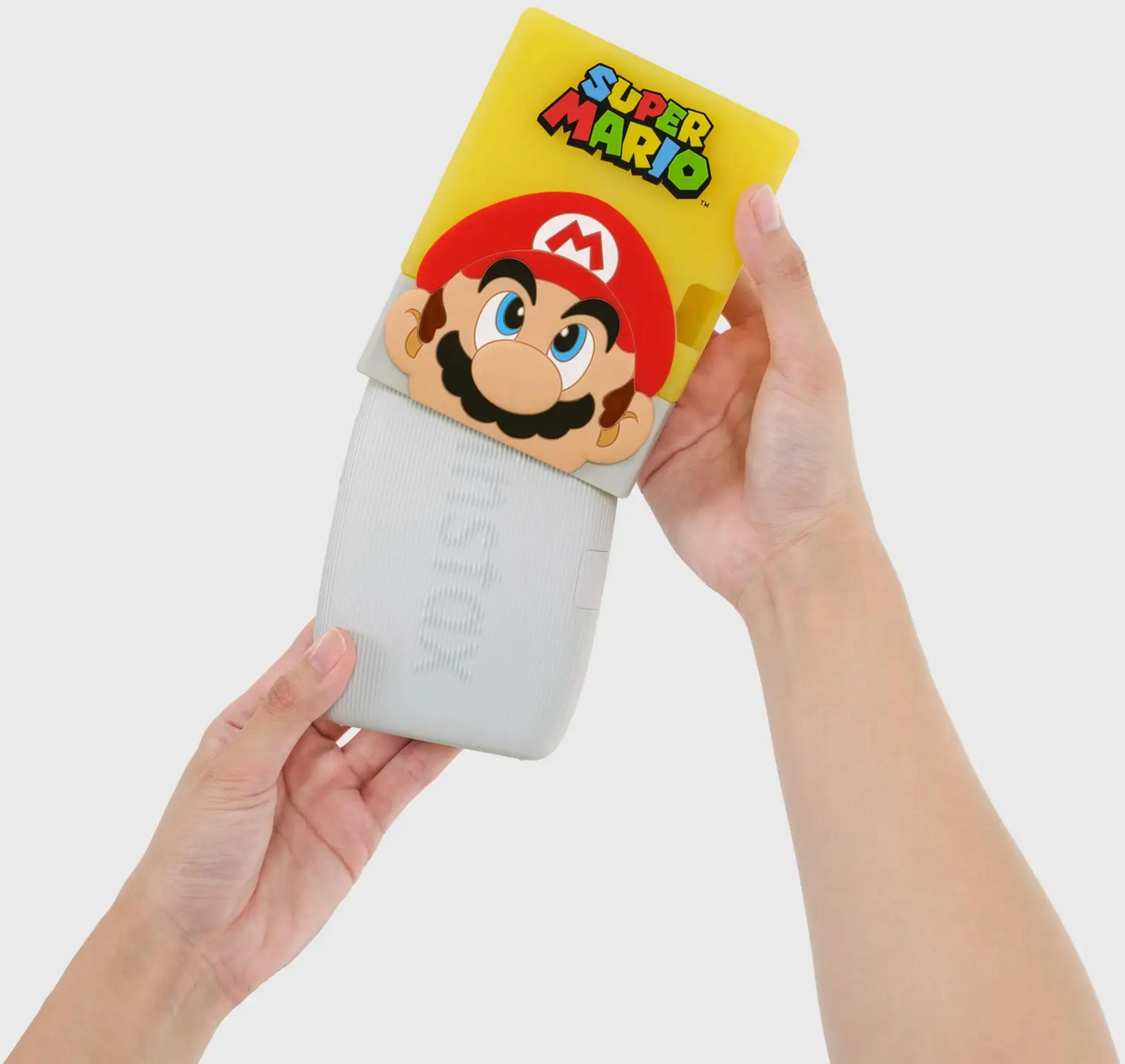 Ręce trzymają żółtą drukarkę Instax Super Mario z motywem Mario.