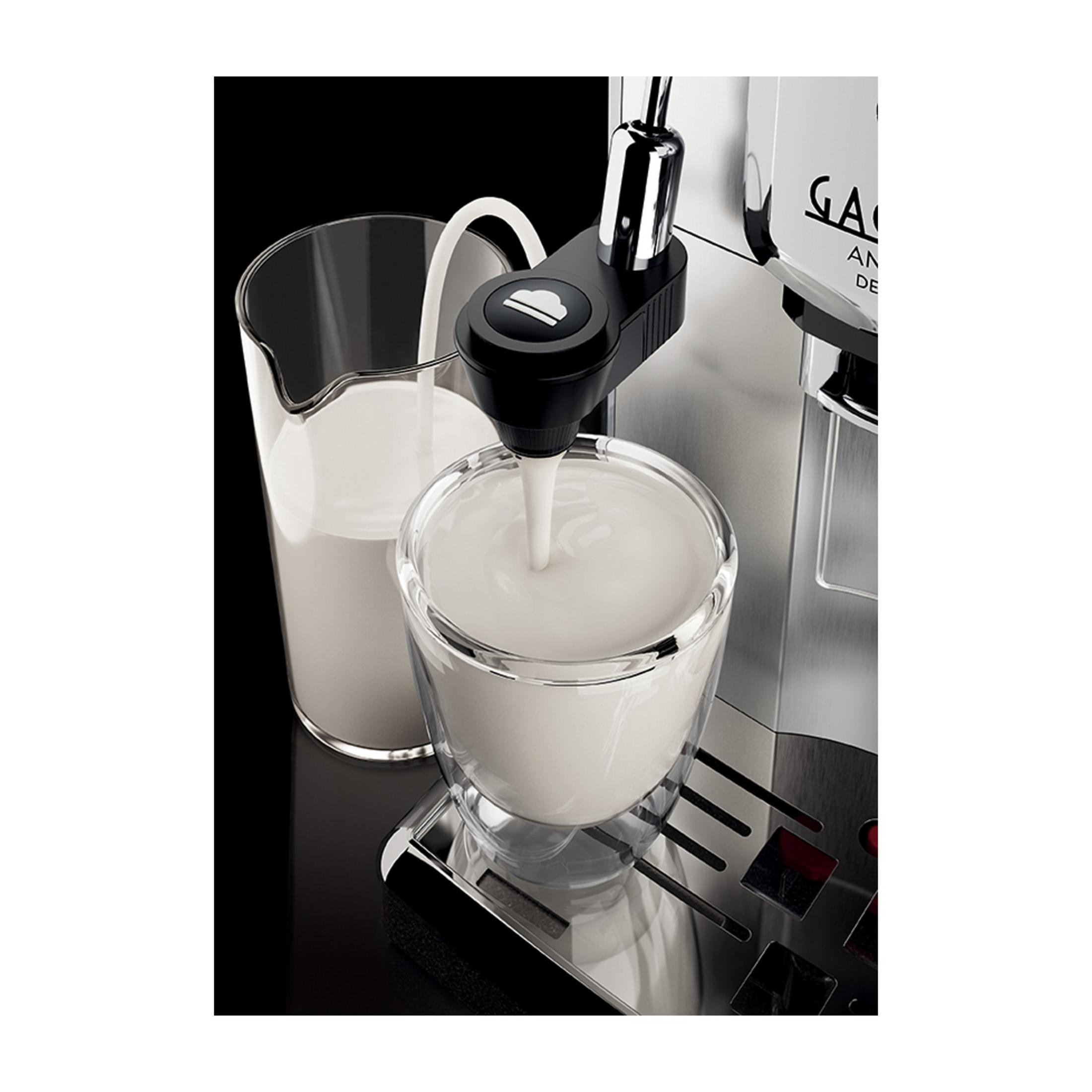 Mleko jest spieniane do przezroczystej szklanki obok dzbanka mleka przez ekspres do kawy.