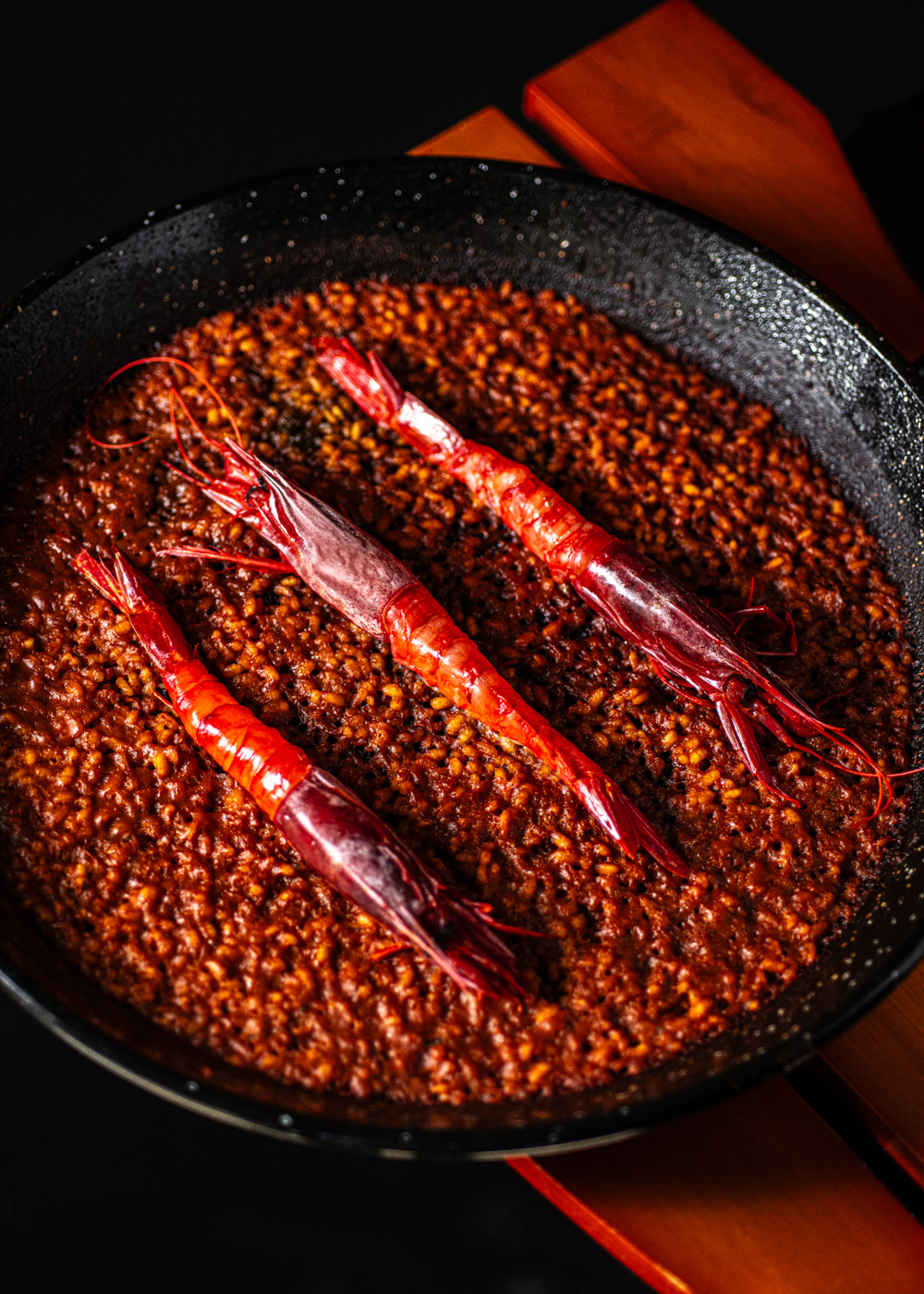 Una paellera negra con tres gambas rojas sobre una mezcla de arroz marrón.