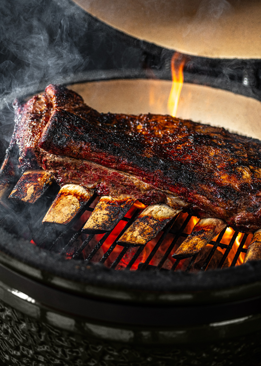 Costillas cocinándose en una parrilla sobre brasas y llamas.