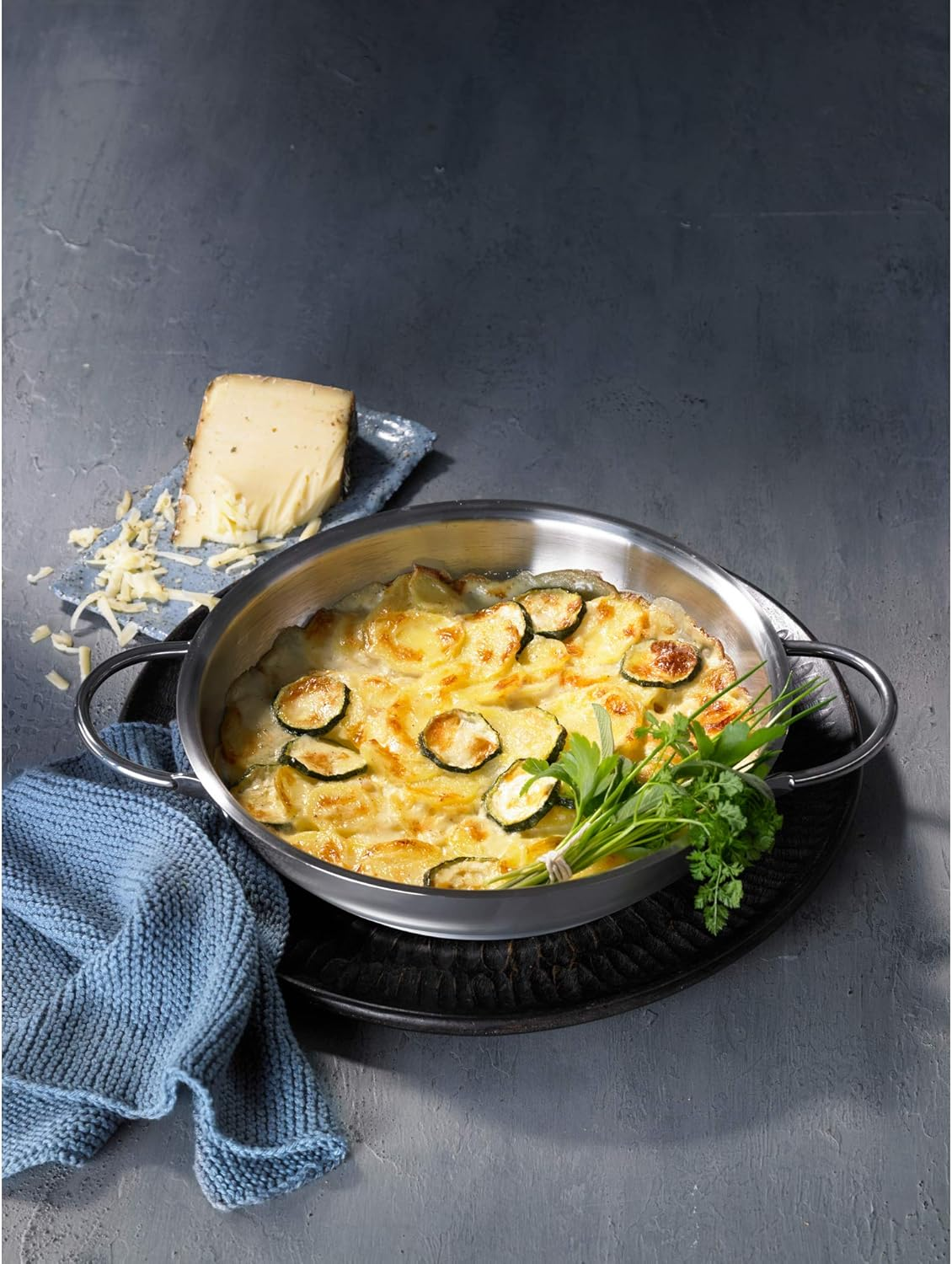 Ein Auflauf mit Kartoffeln, Zucchini und Käse in einer Metallschüssel mit Kräutern.