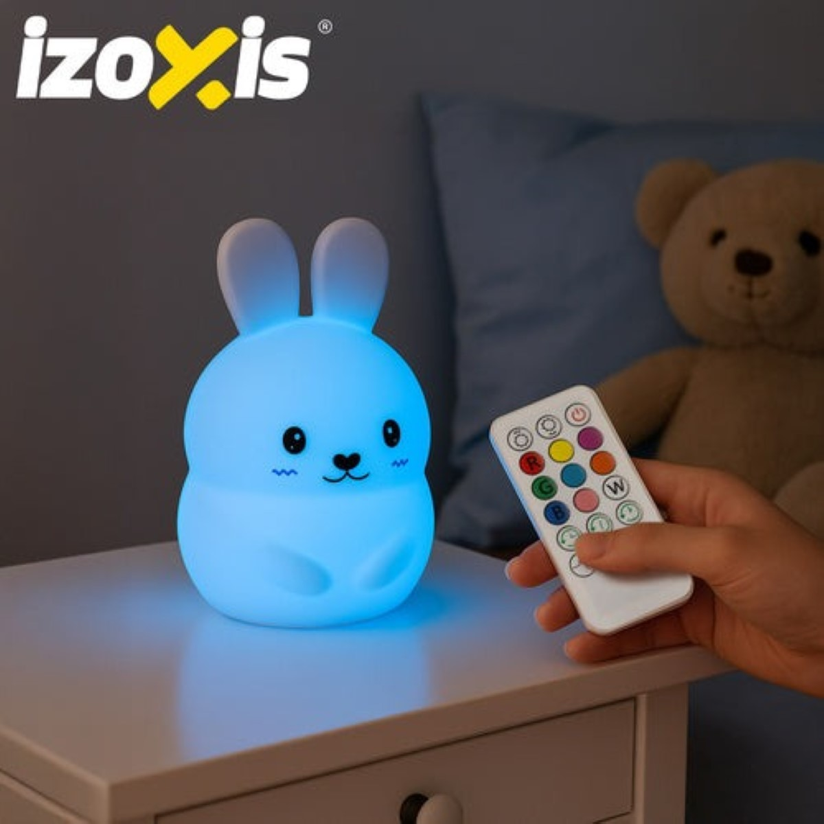 Una lámpara azul de conejito brilla en una mesita de noche junto a un oso de peluche.