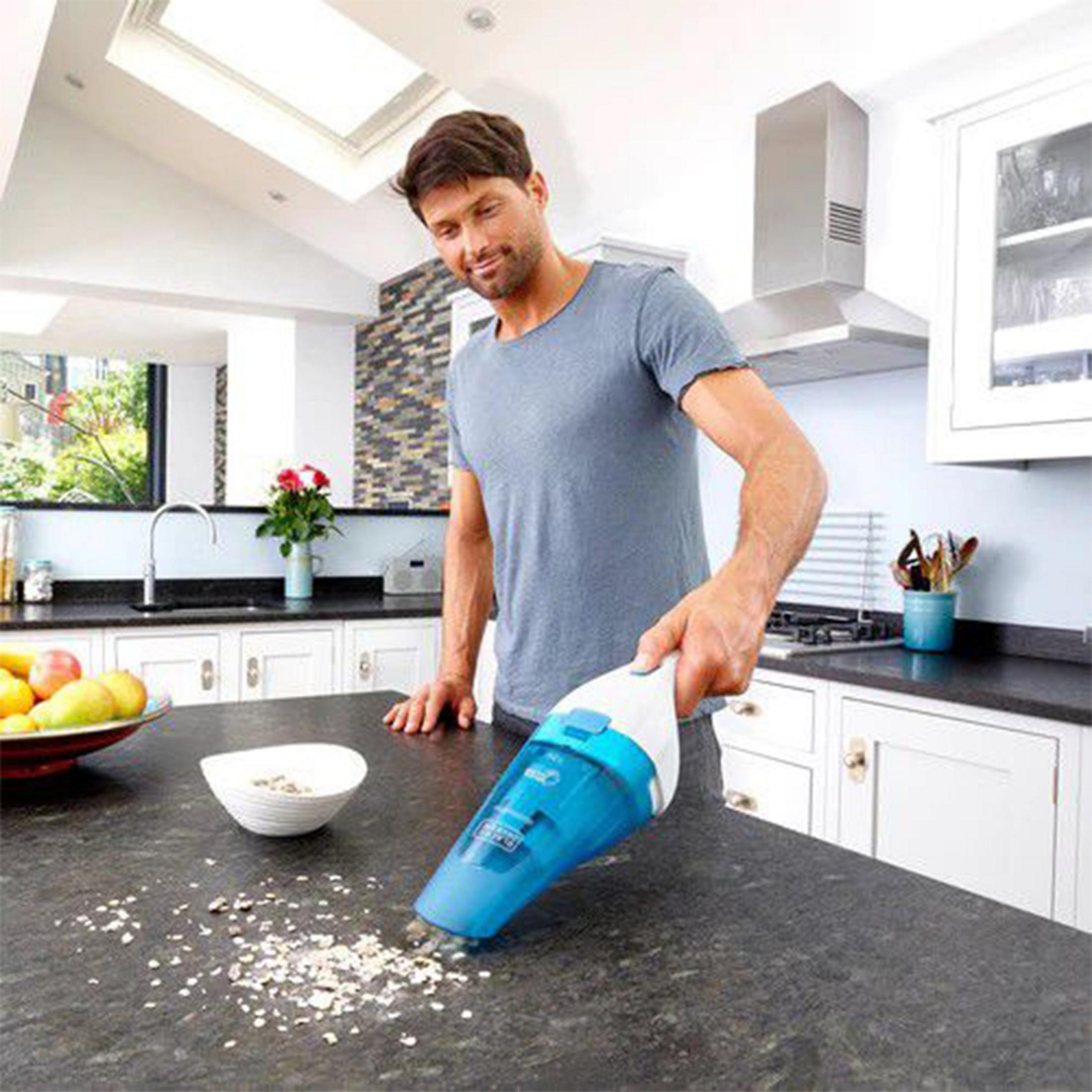 Hombre aspira migas con aspiradora azul de mano en encimera de cocina.