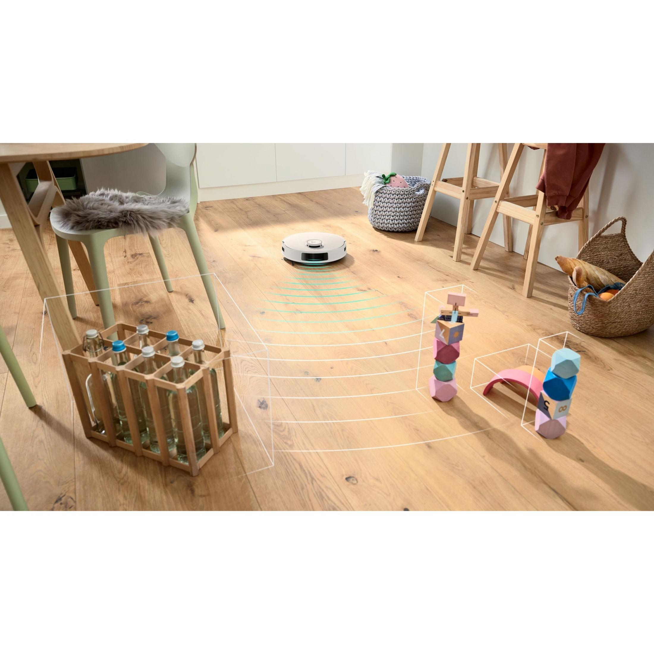 A robot vacuum navigates a wooden floor between bottles and toys.