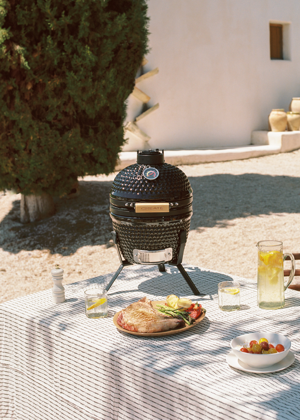 Una parrilla negra sobre una mesa con un bistec, verduras y bebidas al aire libre.