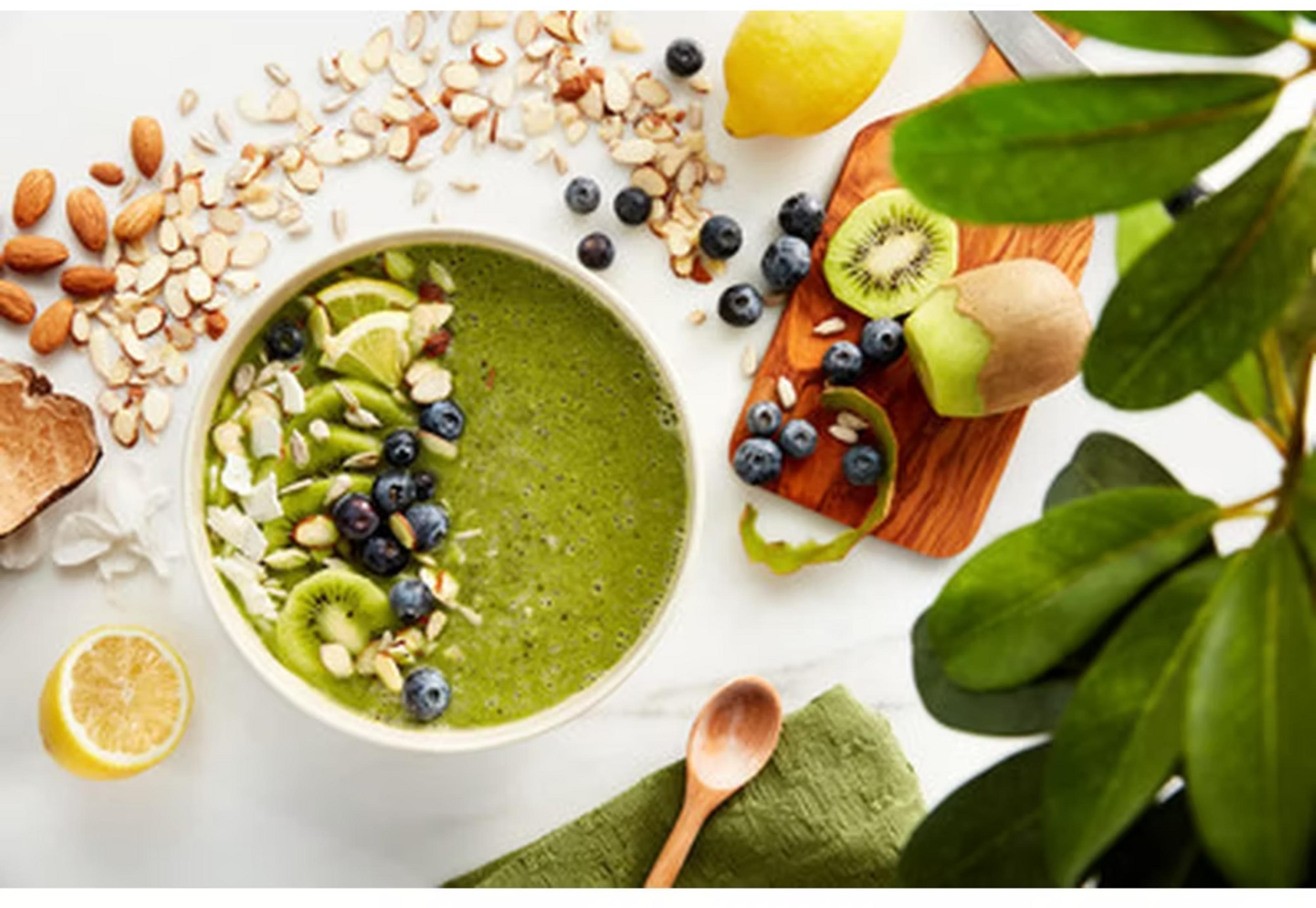 Grüner Smoothie in Schale mit Beeren, Kiwi, Mandeln und Zitrone.