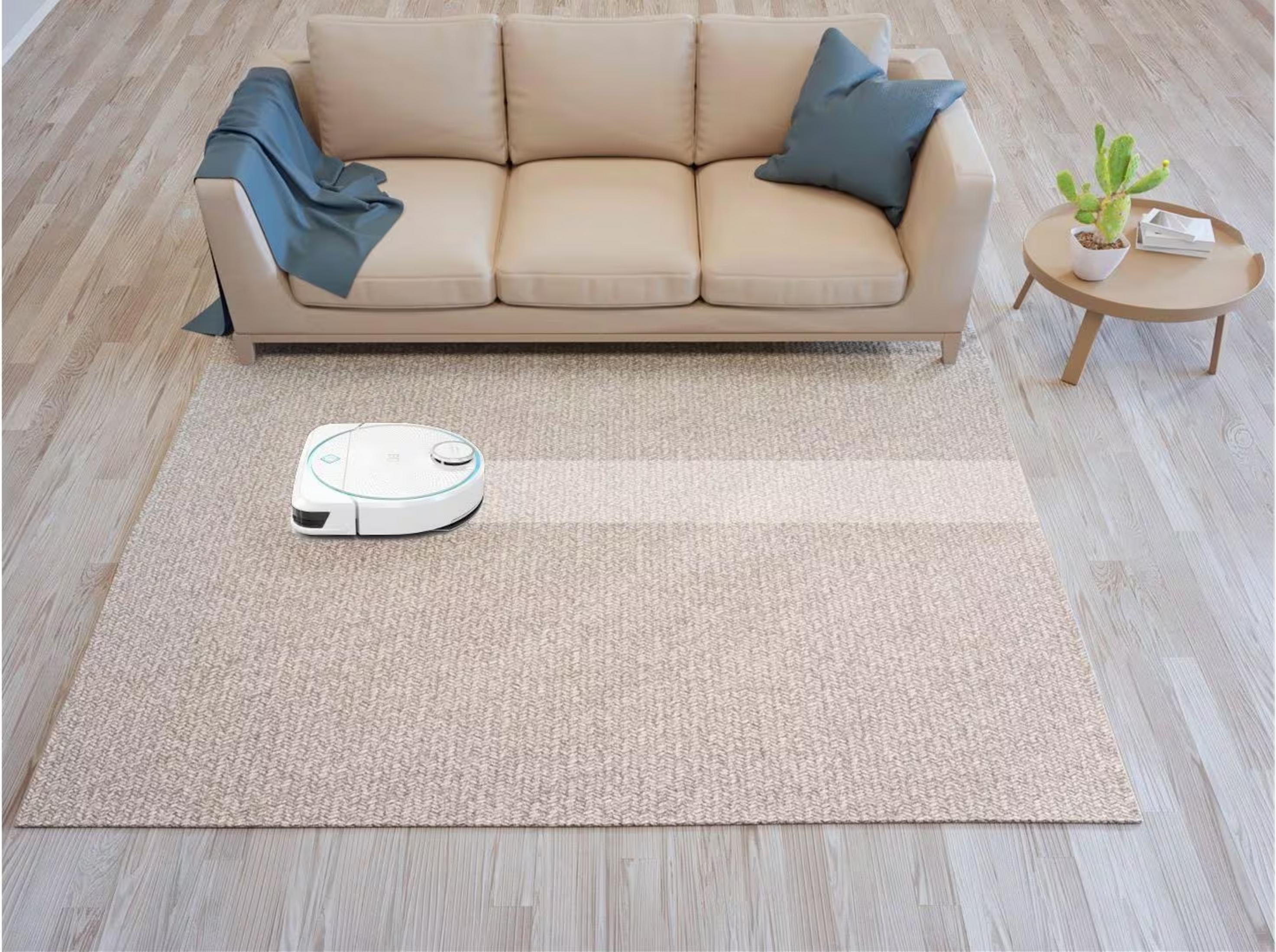 Ein weißer Saugroboter reinigt einen Teppich vor einem beigen Sofa.