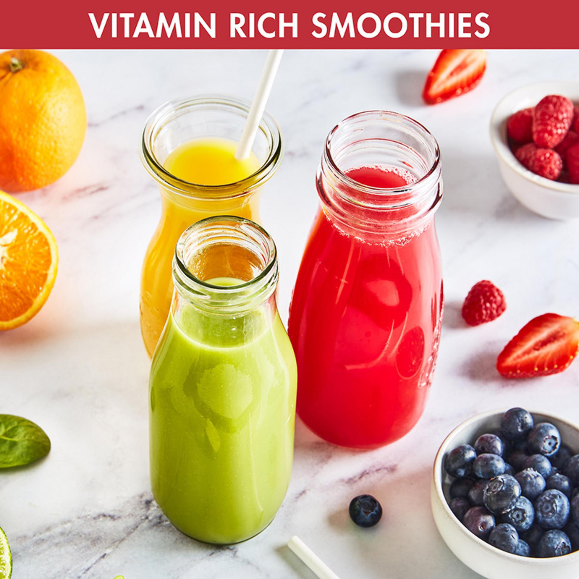 Drei Flaschen mit bunten Smoothies neben Früchten wie Orangen, Erdbeeren und Beeren.