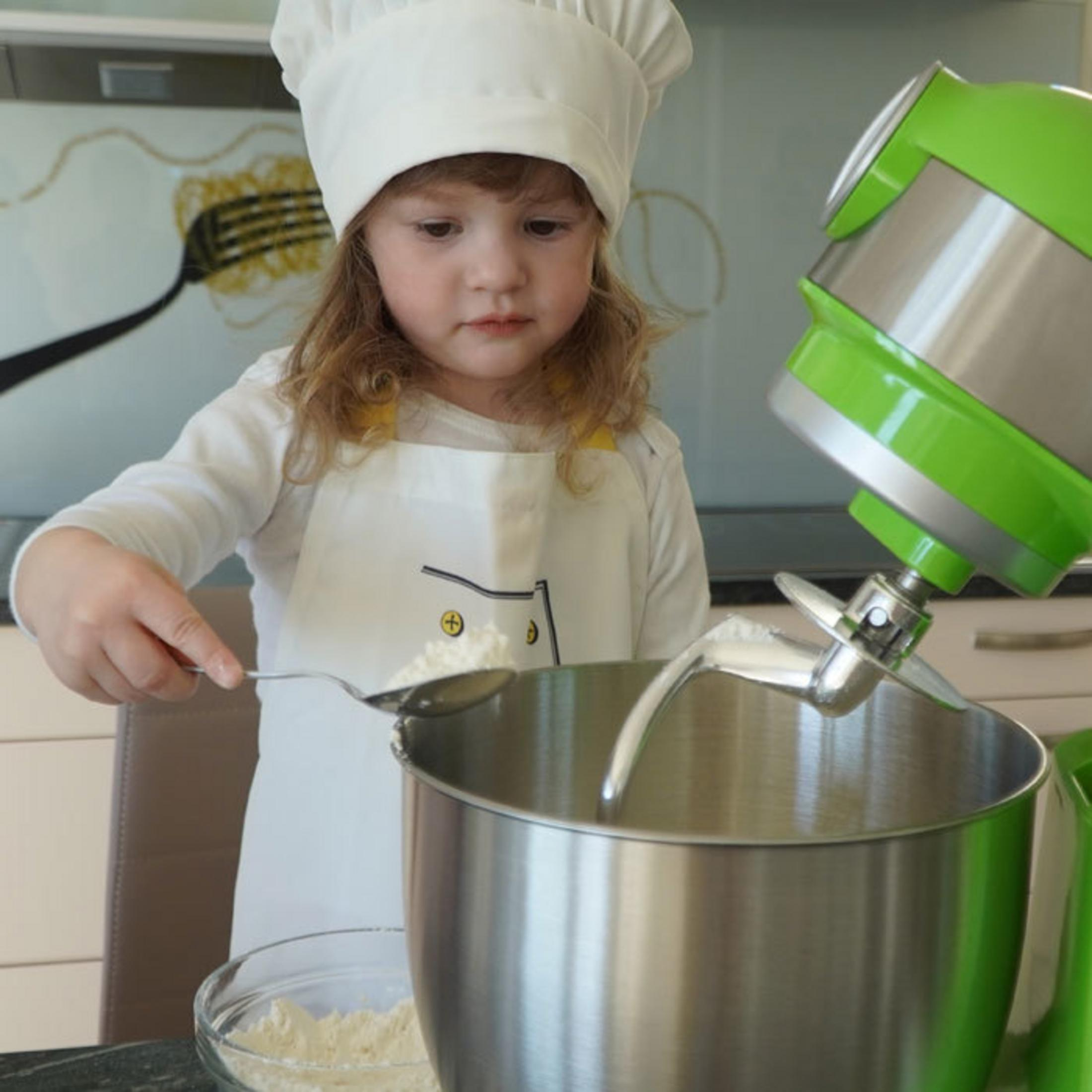 Un bambino piccolo in abiti da chef aggiunge farina a una planetaria con un cucchiaio.