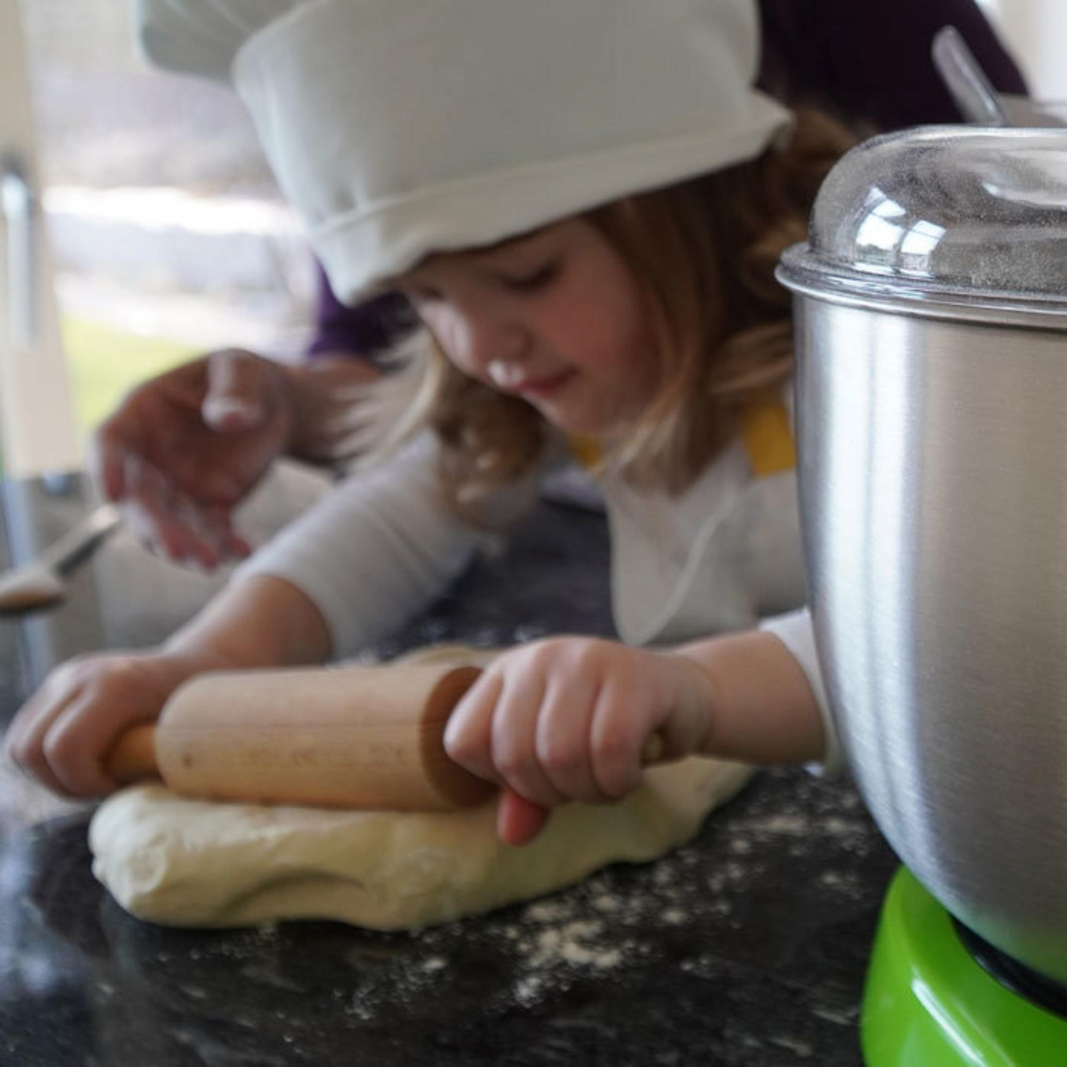 Un bambino con cappello da chef stende la pasta con mattarello.