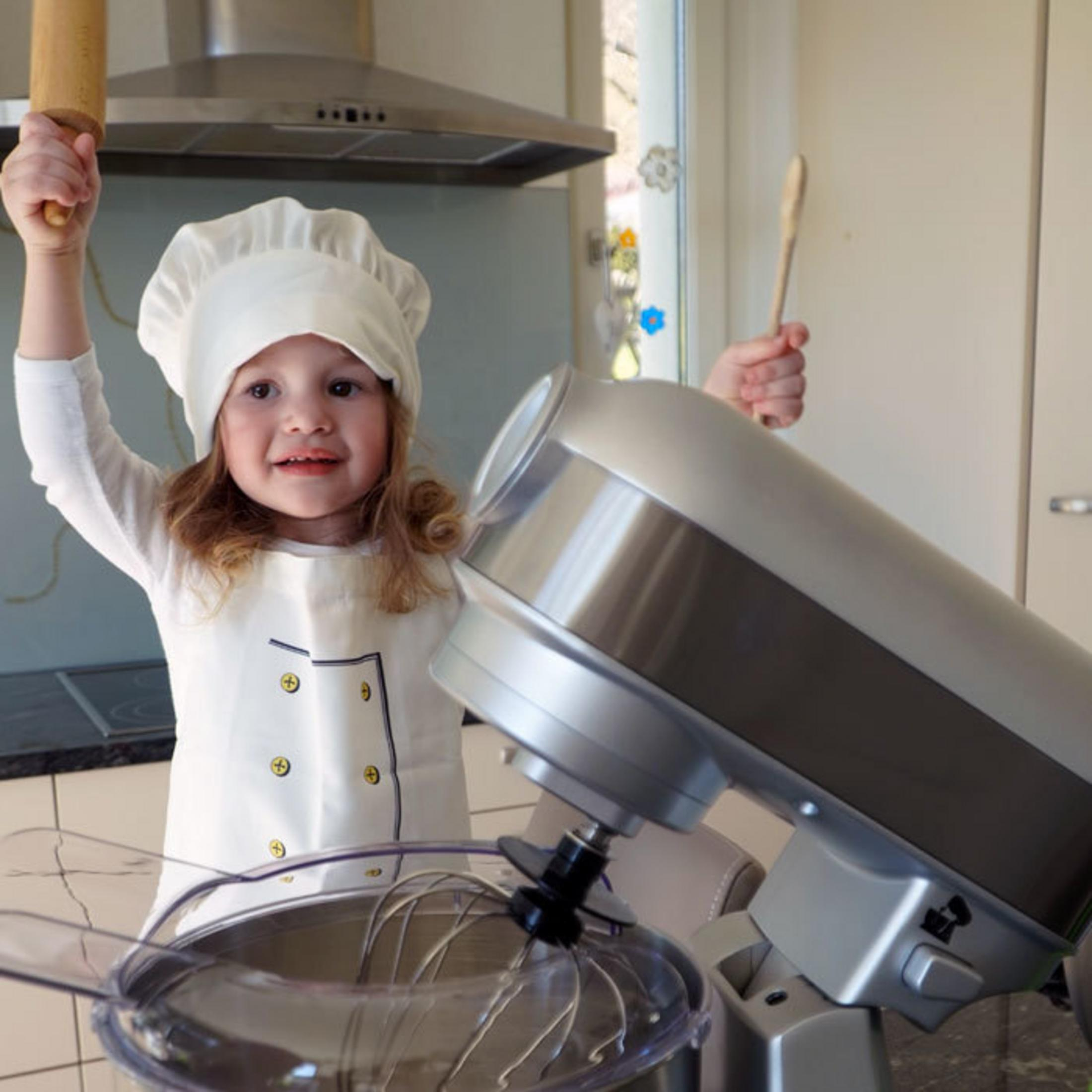 Un bambino in tenuta da chef tiene un mattarello e un cucchiaio di legno.