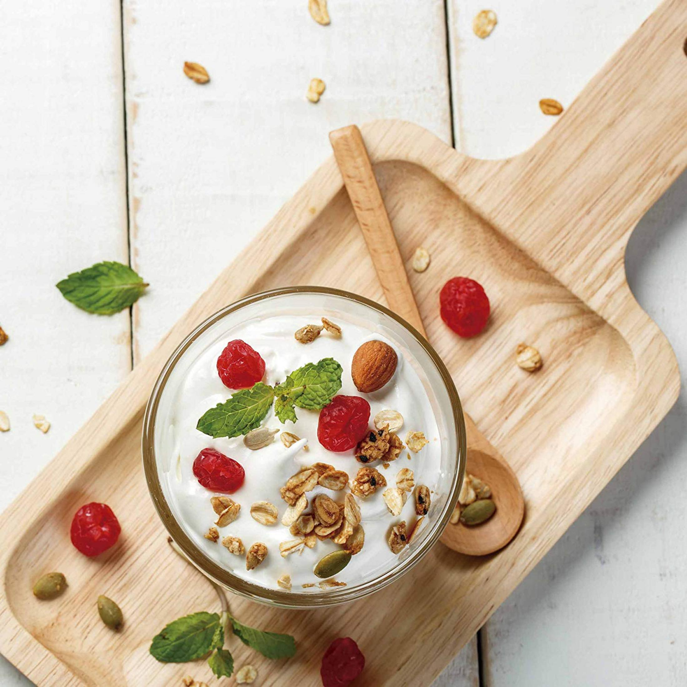 Yogurt con granola, bacche e noci su un vassoio di legno.