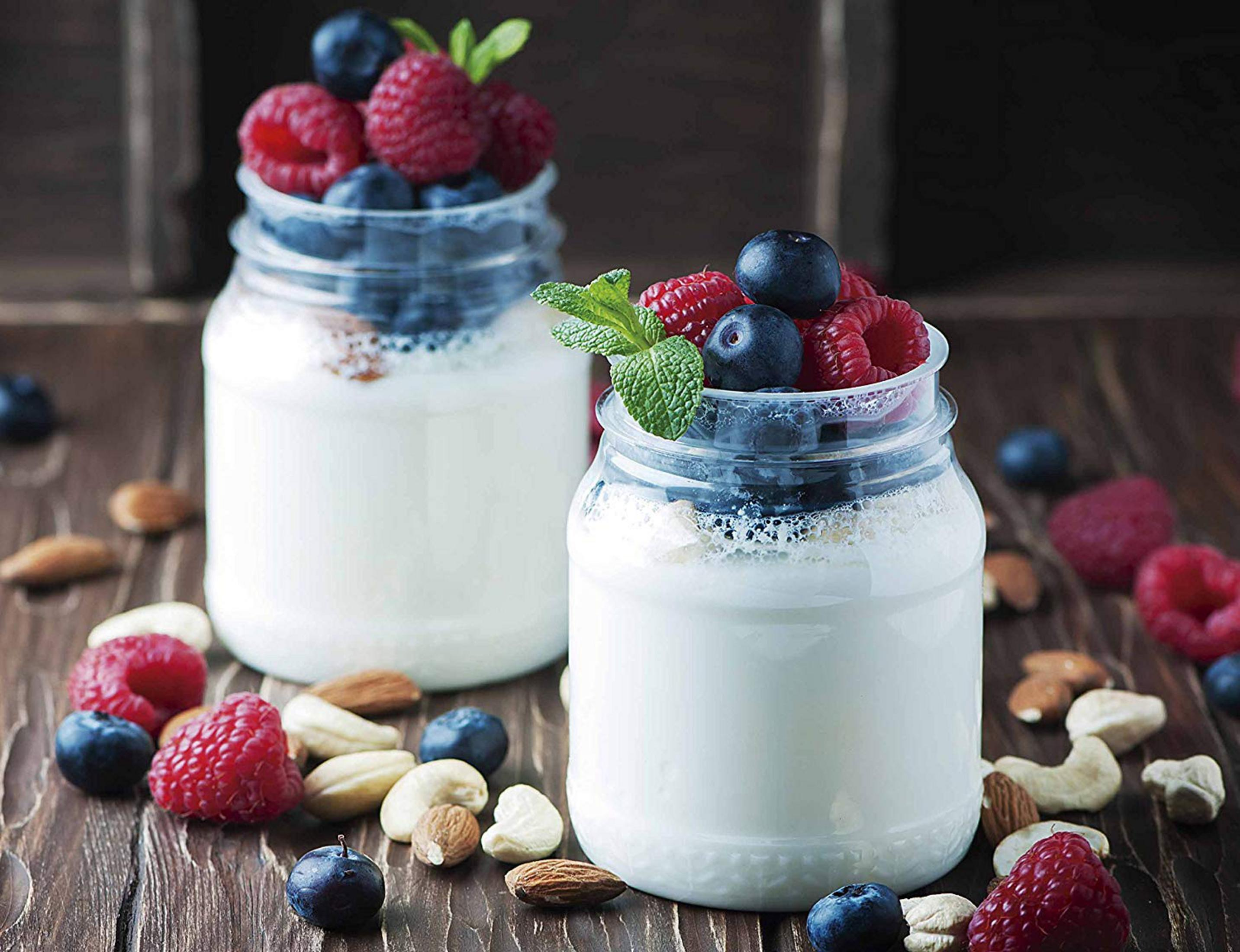 Due vasetti di yogurt con bacche e noci su una superficie di legno.
