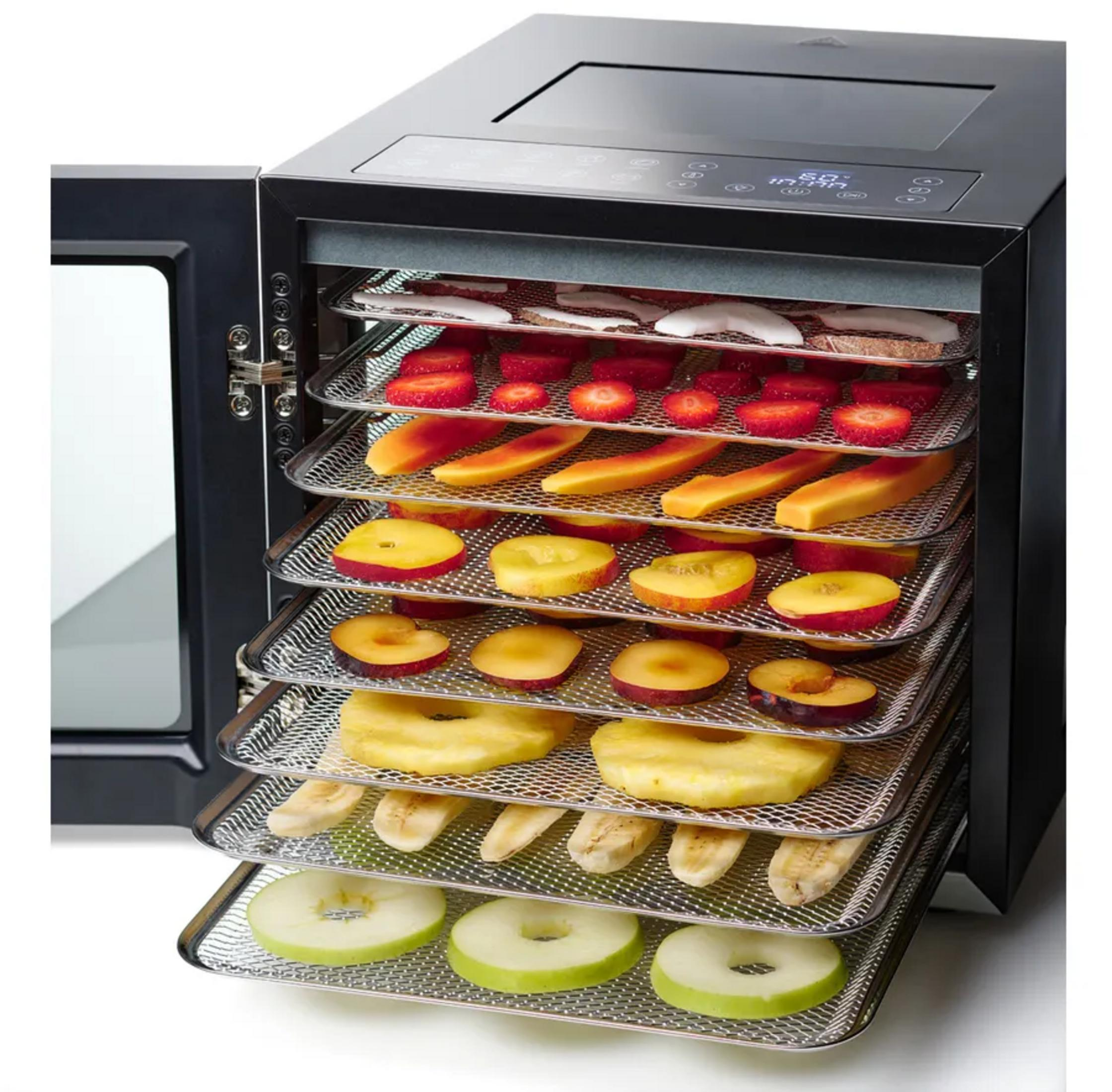 Ein schwarzer Dörrautomat mit geöffneter Tür, gefüllt mit Obst.