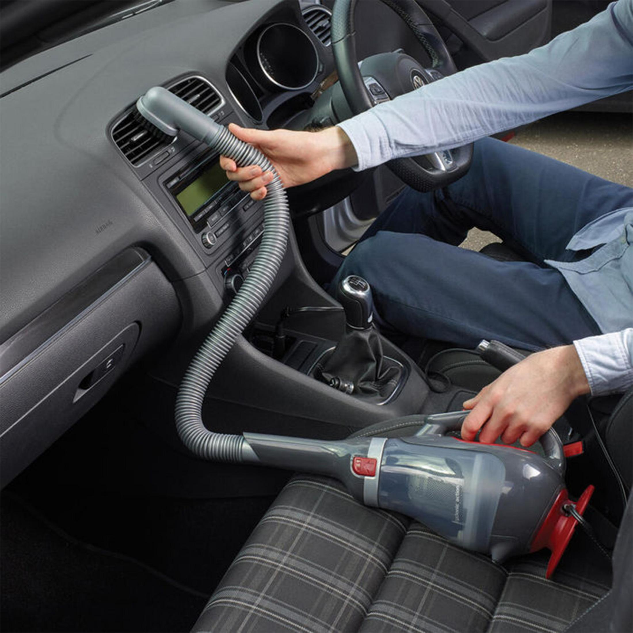 Osoba czyści wnętrze samochodu podręcznym odkurzaczem skierowanym na siedzenie.