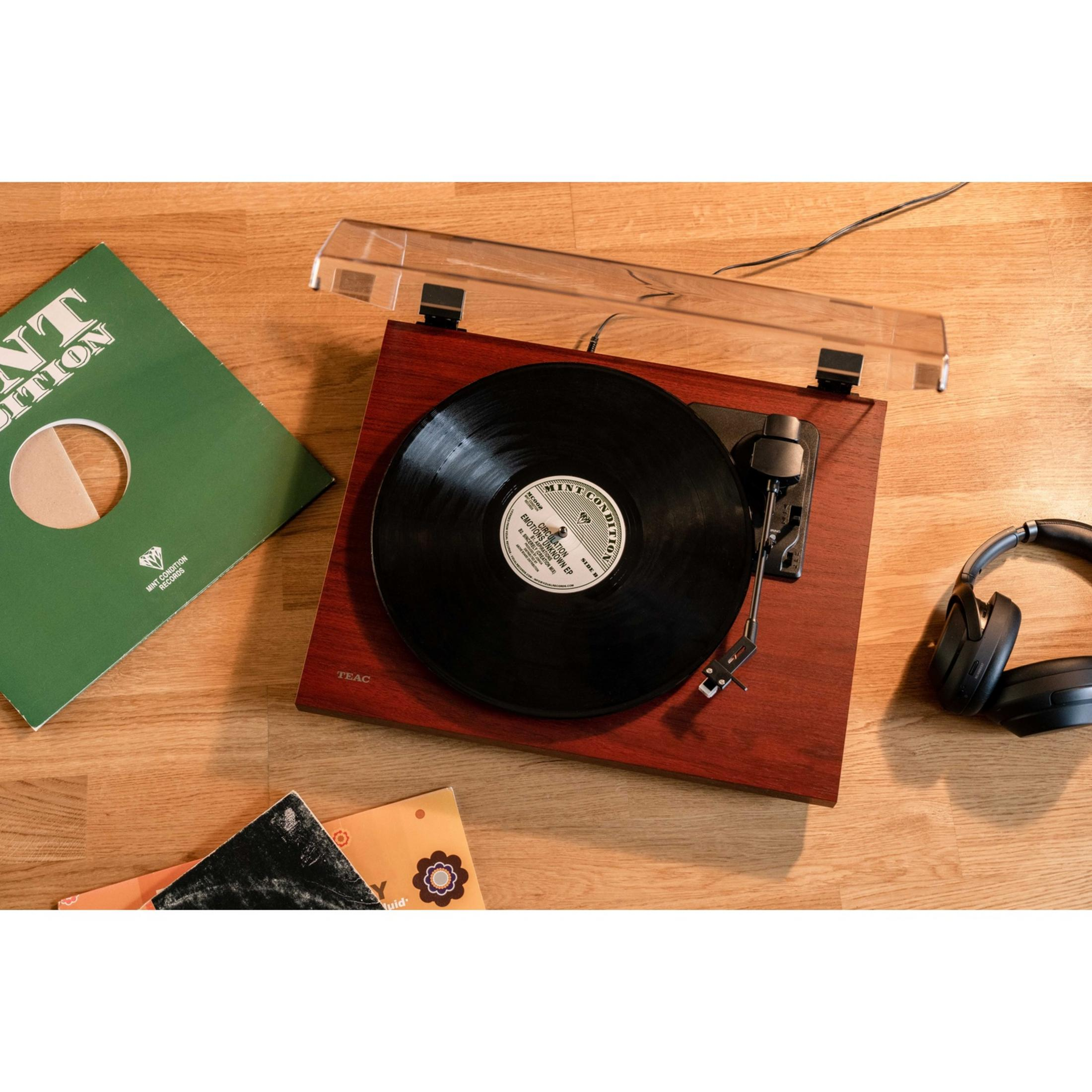 Une platine vinyle avec un disque, des écouteurs et des pochettes sur un sol en bois.