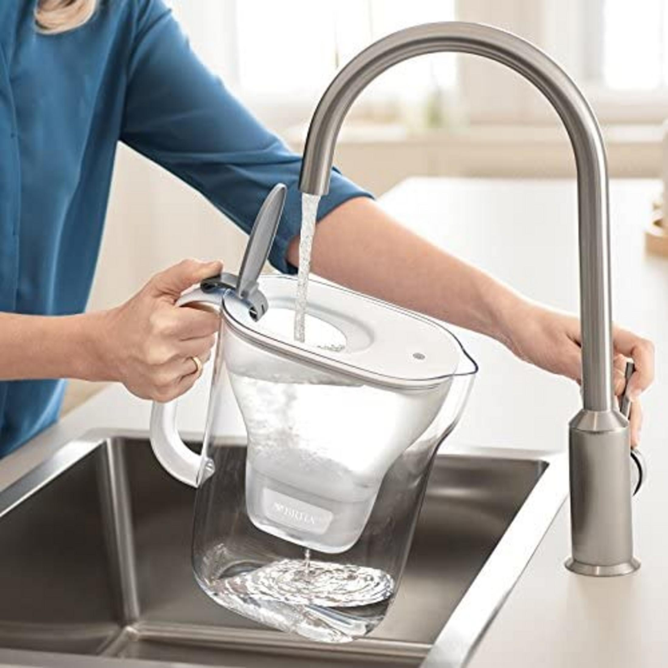 Una persona riempie una caraffa filtrante Brita sotto un rubinetto in un lavello.