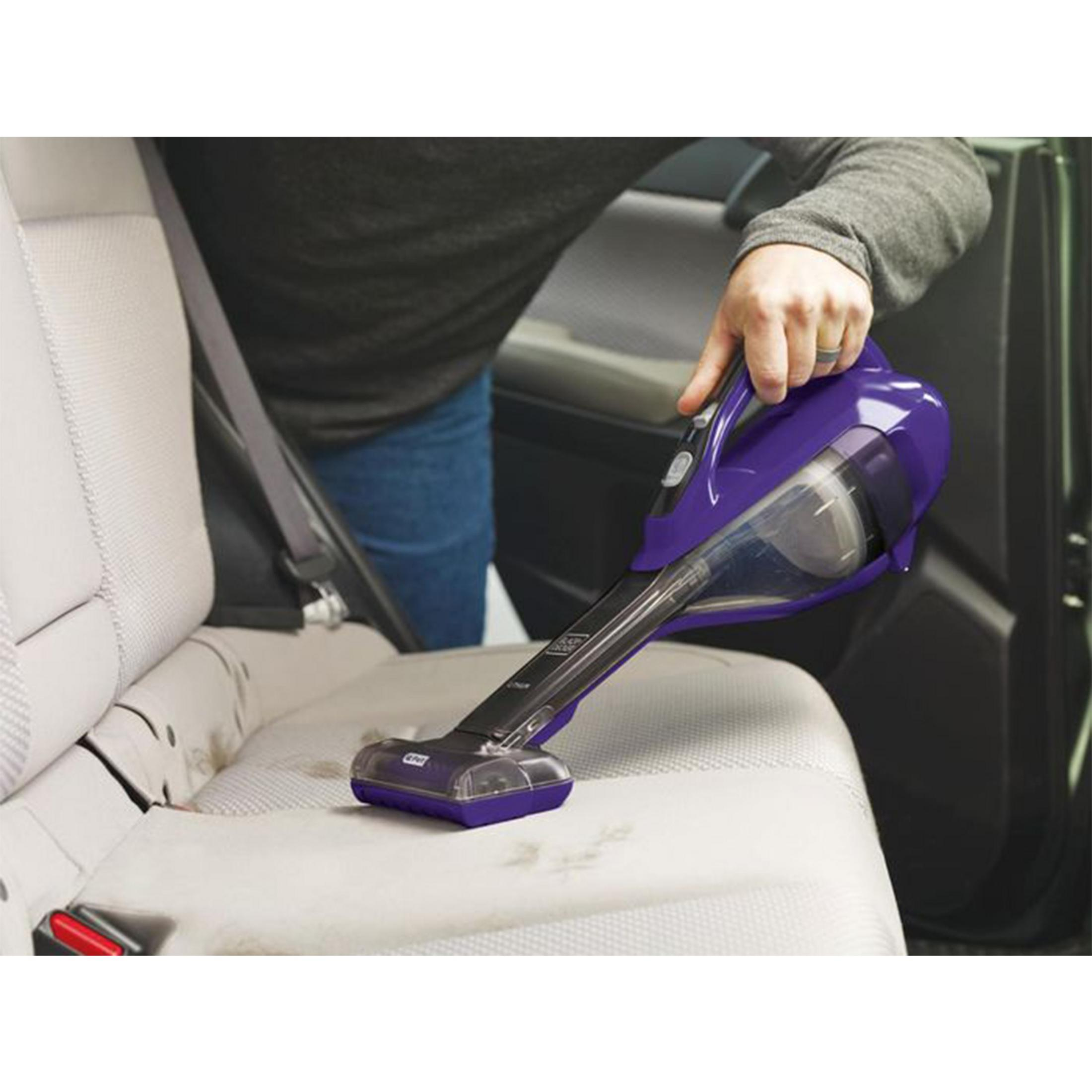 Persona limpiando asiento de coche con aspiradora morada.