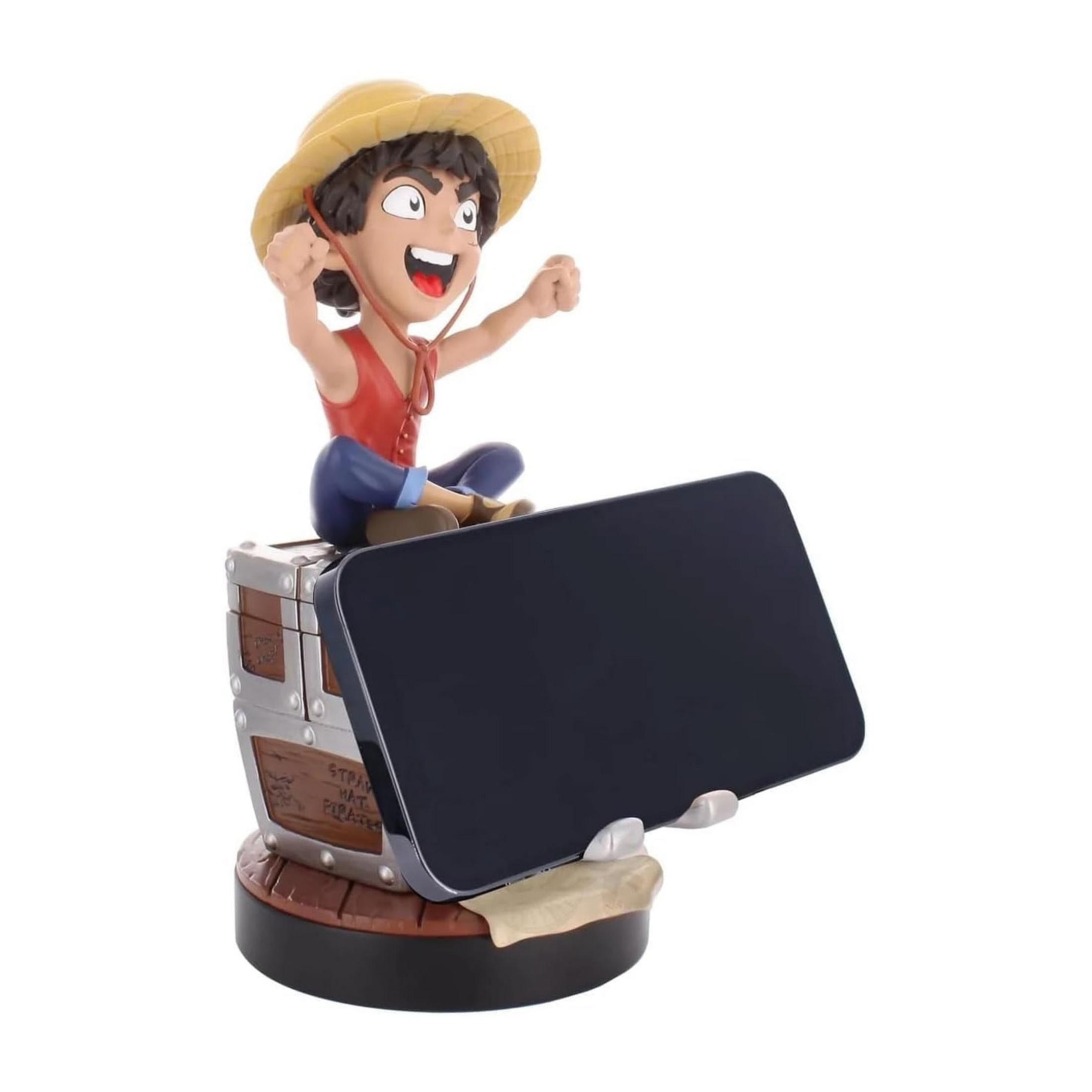 Una figura anime con cappello di paglia seduta su un baule, tiene uno smartphone.