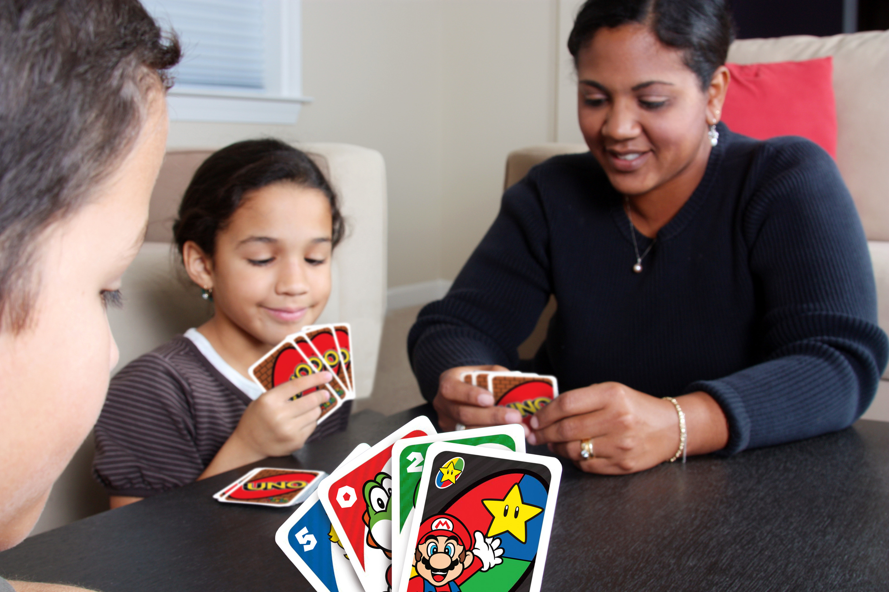Trois personnes jouent aux cartes UNO. Des cartes Mario au premier plan.