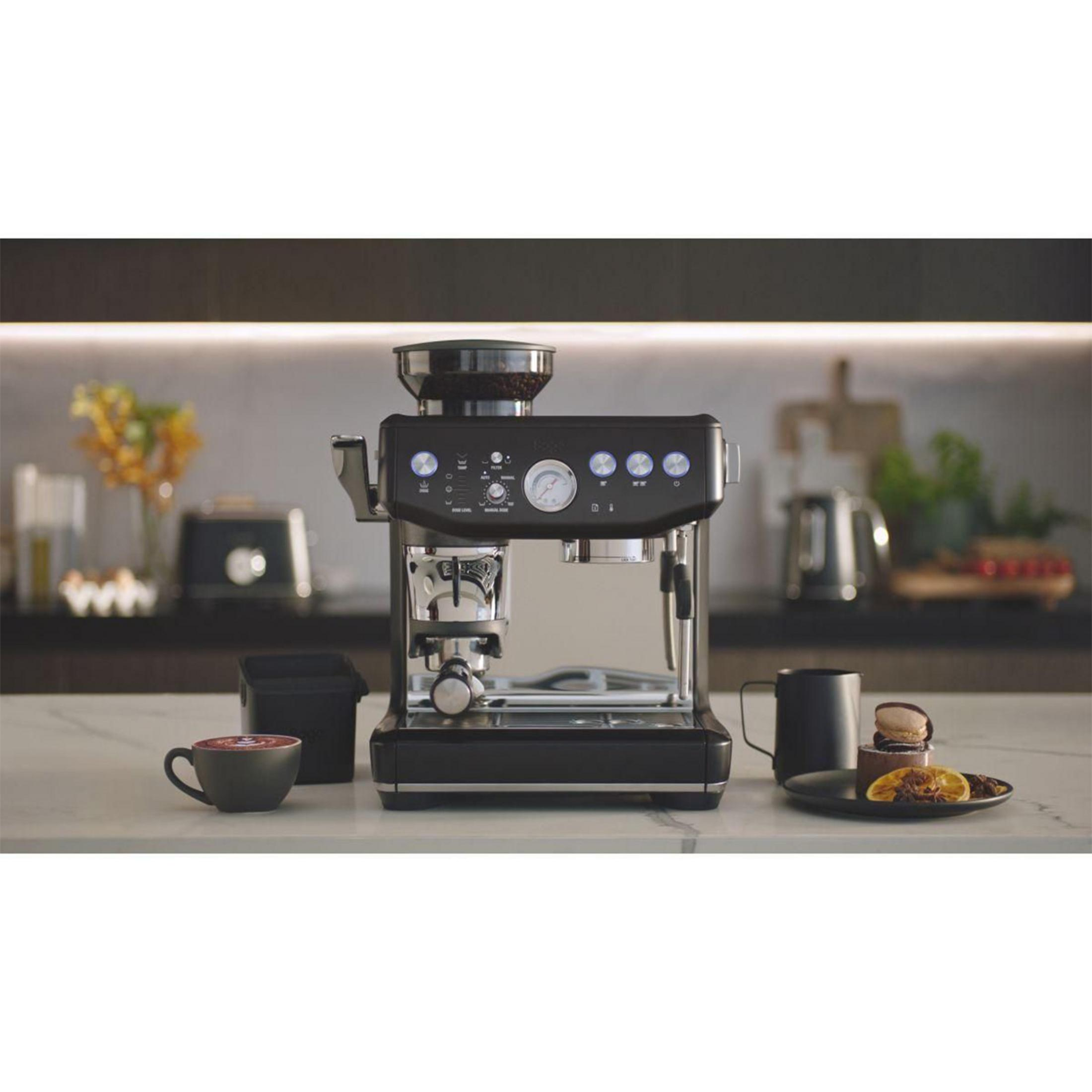 Eine schwarze Kaffeemaschine mit Kaffeetasse, Makronen und einer Scheibe Orange.