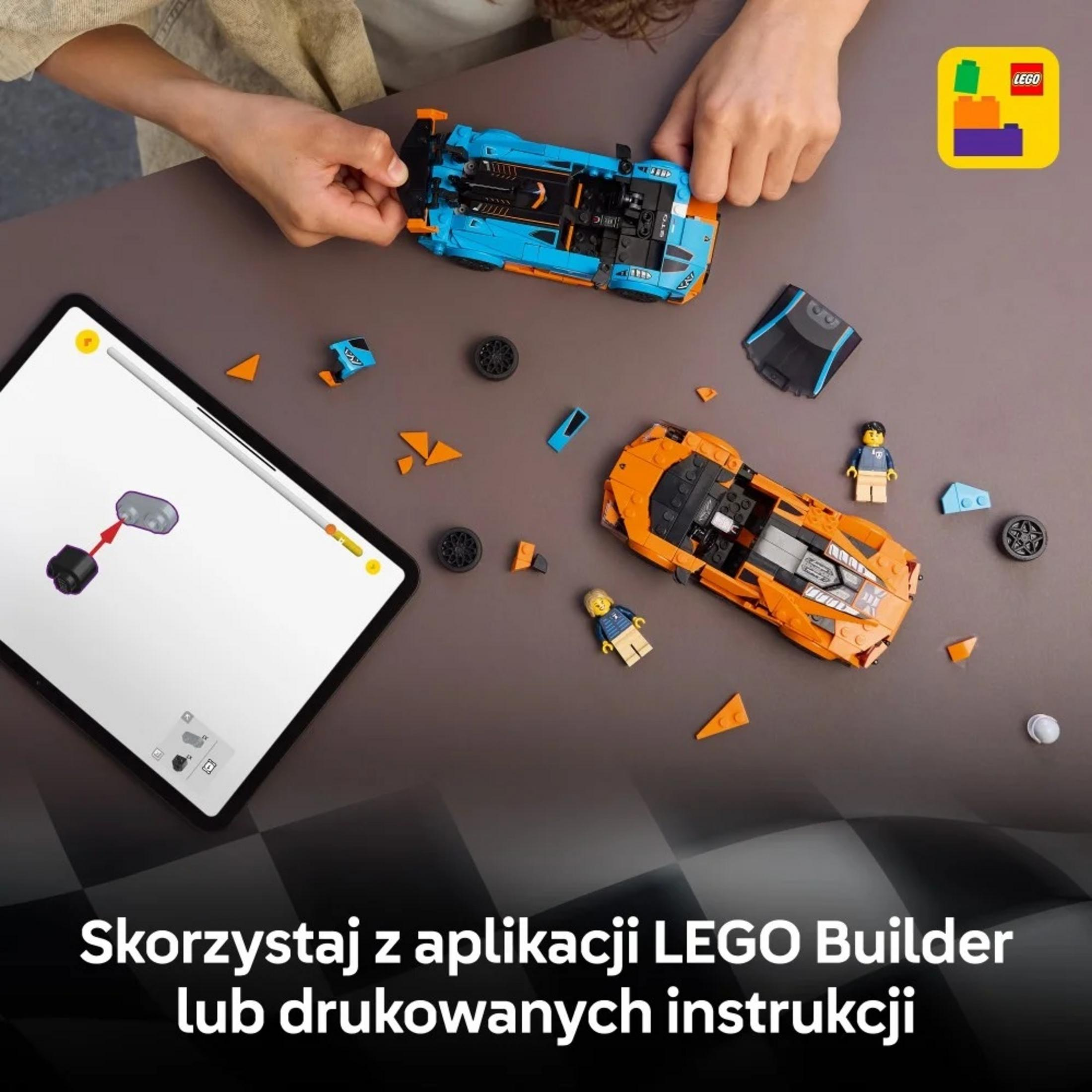 Dwa samochody Lego, niebieski i pomarańczowy, na stole obok tabletu i części.