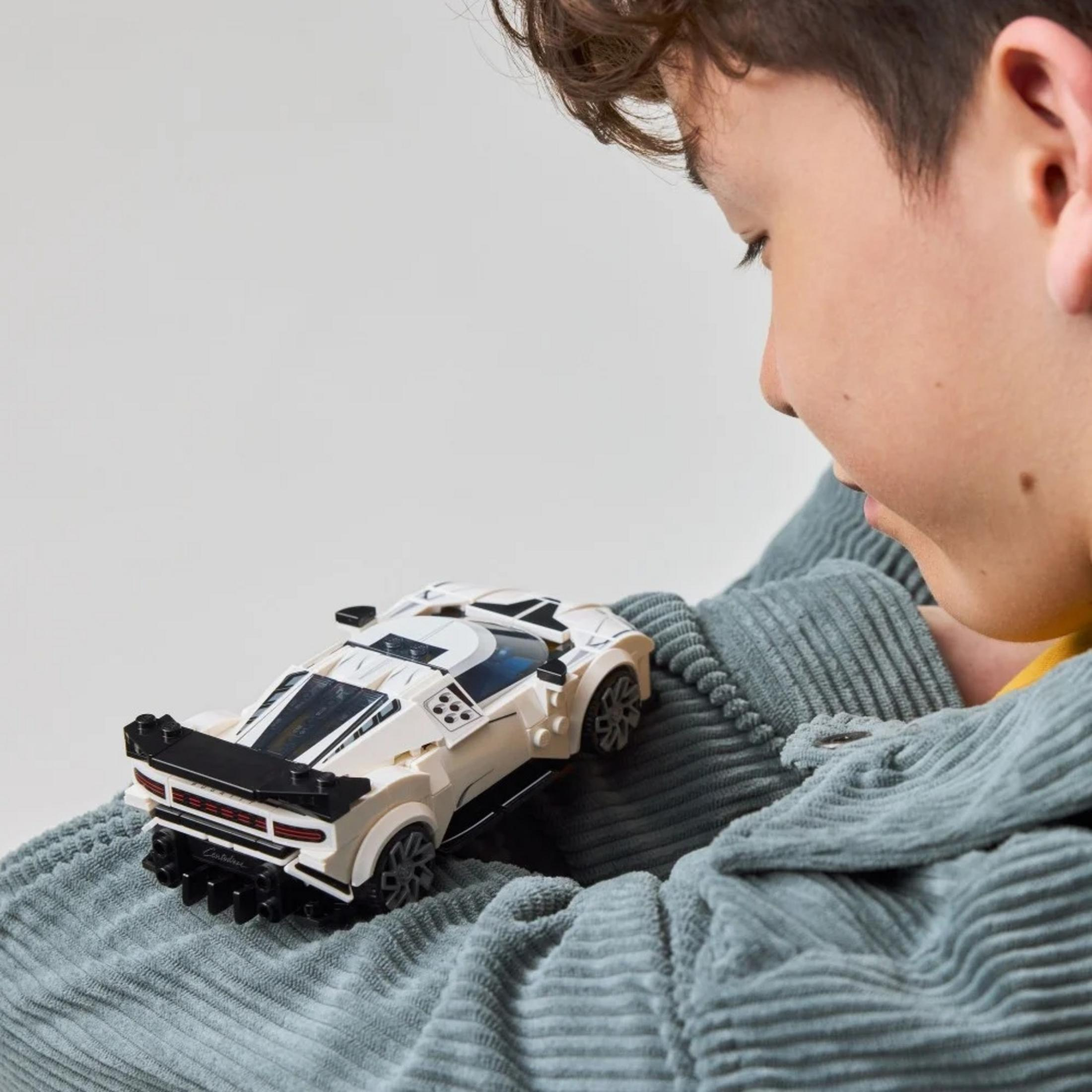 Chłopiec trzyma na kolanach biały samochód z klocków na szarej tkaninie.