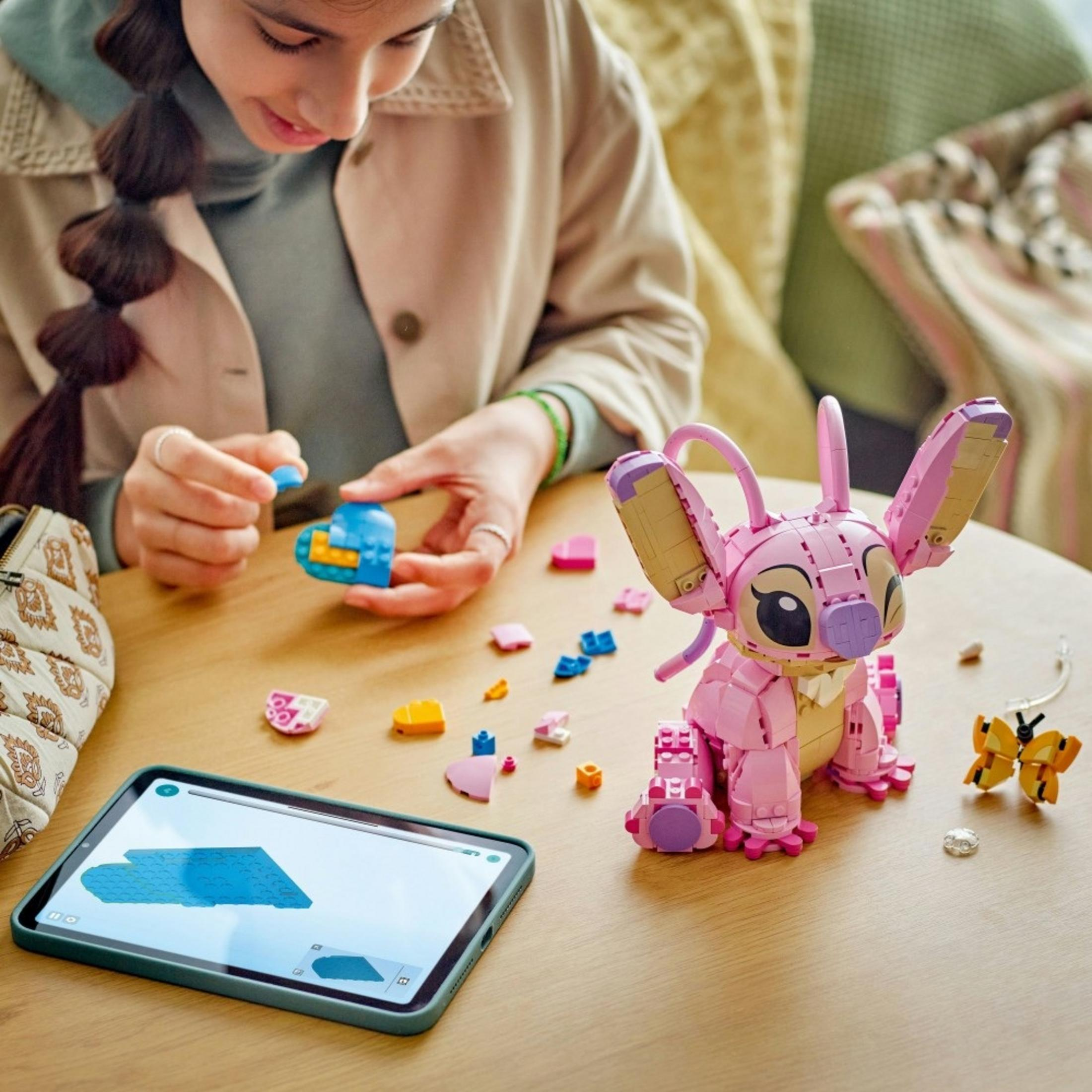 Dziewczyna buduje różową postać z Lego z instrukcjami na tablecie.