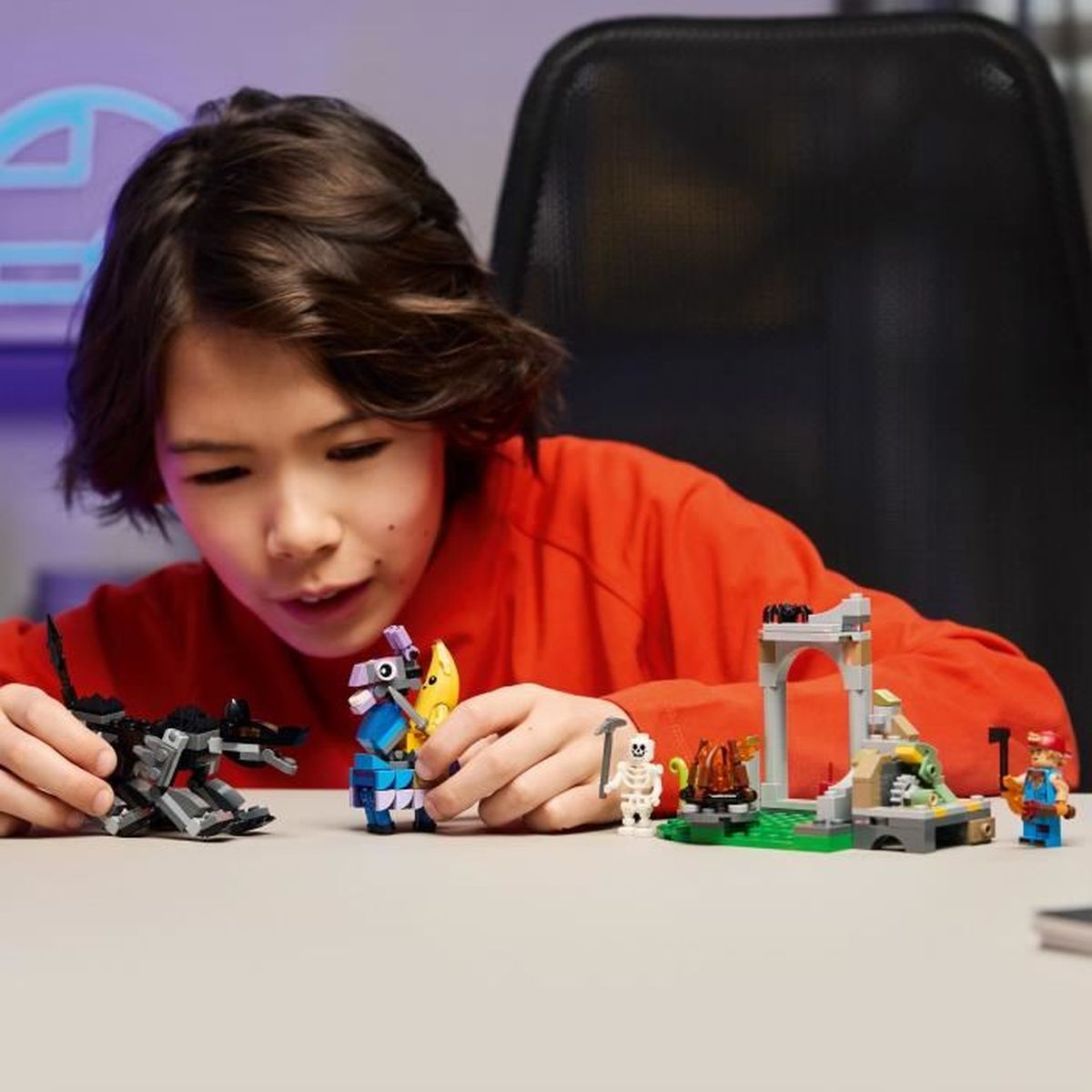 Bir çocuk, siyah bir ejderha ve bir iskelet dahil renkli Lego figürleriyle inşa ediyor.
