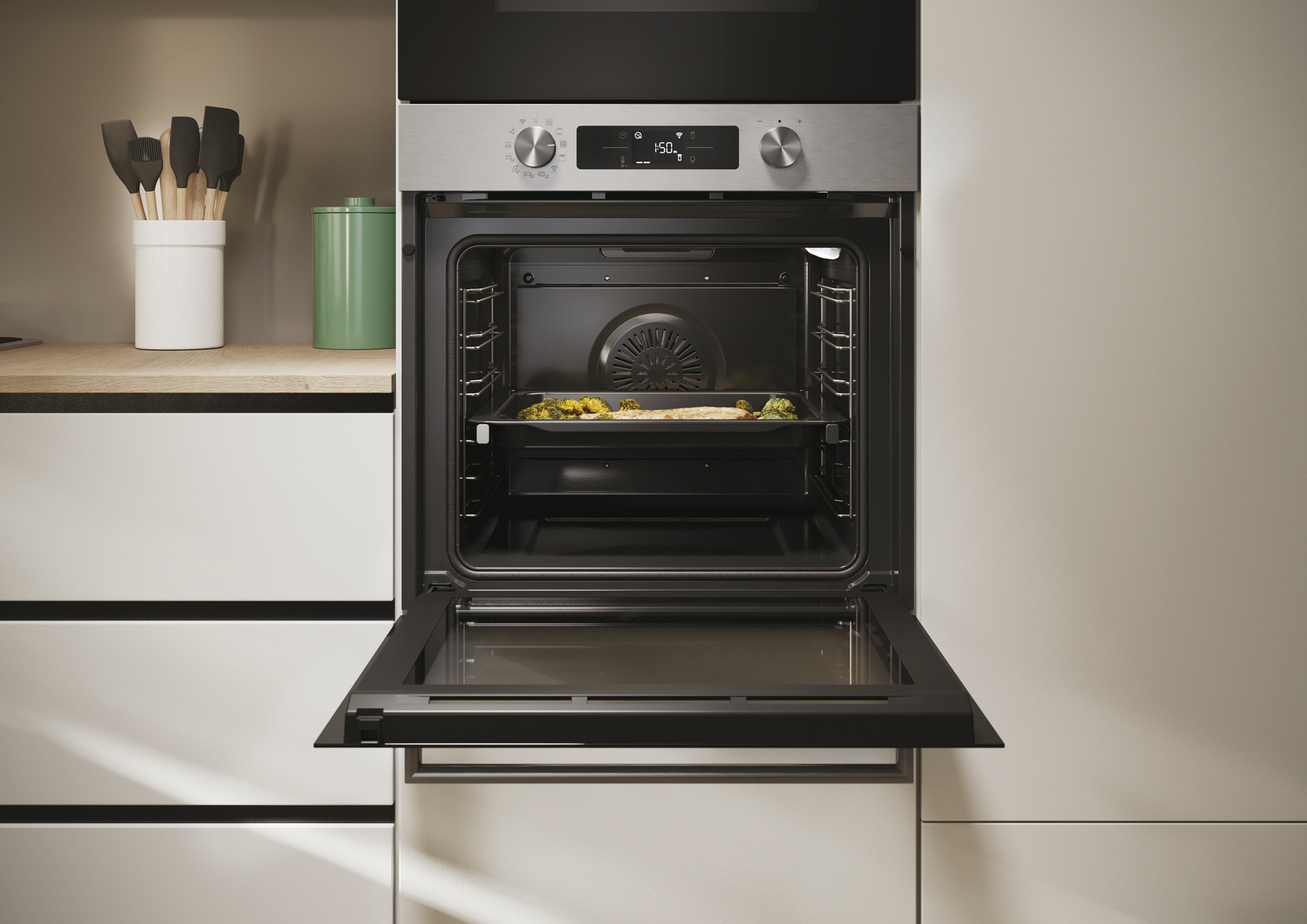 Forno aperto con cibo in teglia, utensili da cucina nelle vicinanze.