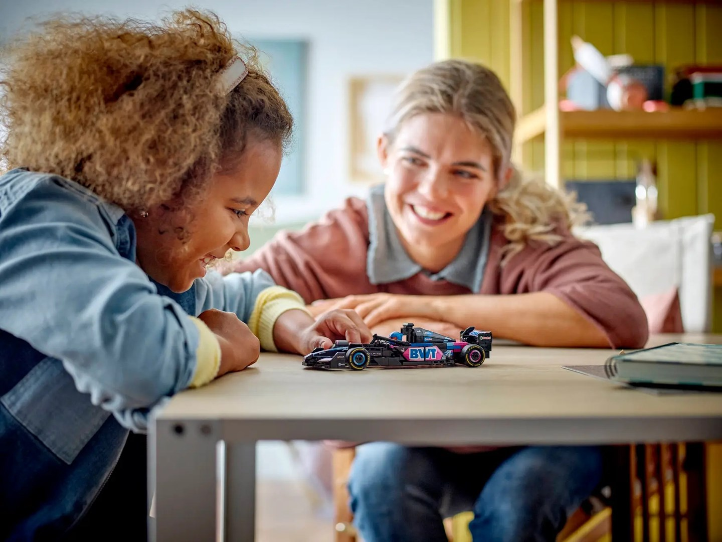Dziewczynka i kobieta uśmiechają się nad zabawką-samochodem na stole.
