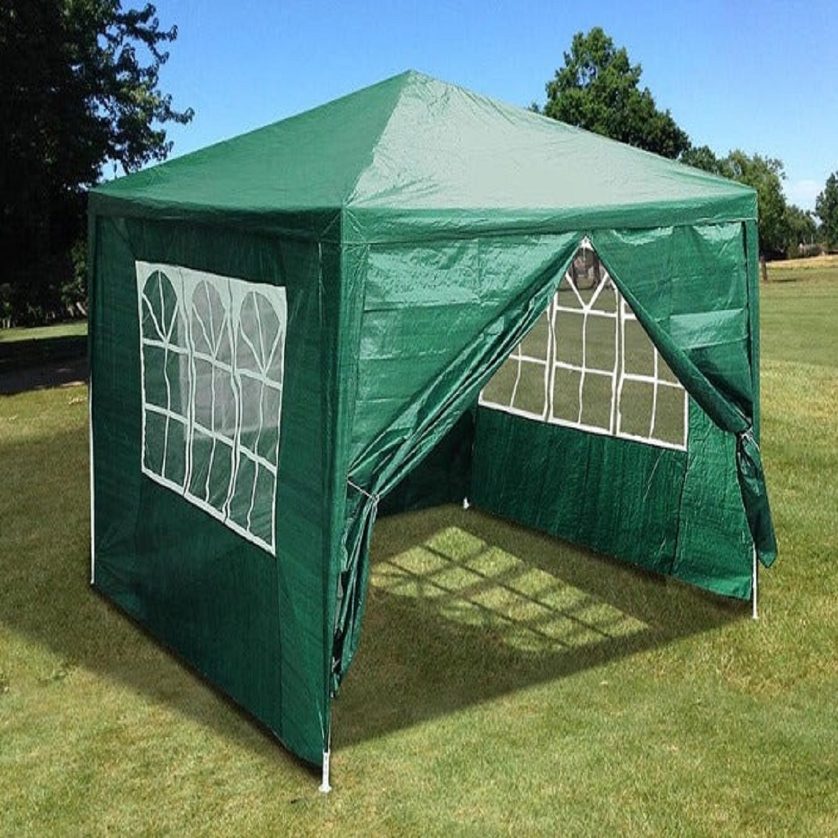 Una carpa verde con ventanas se encuentra en un campo de césped bajo un cielo azul.