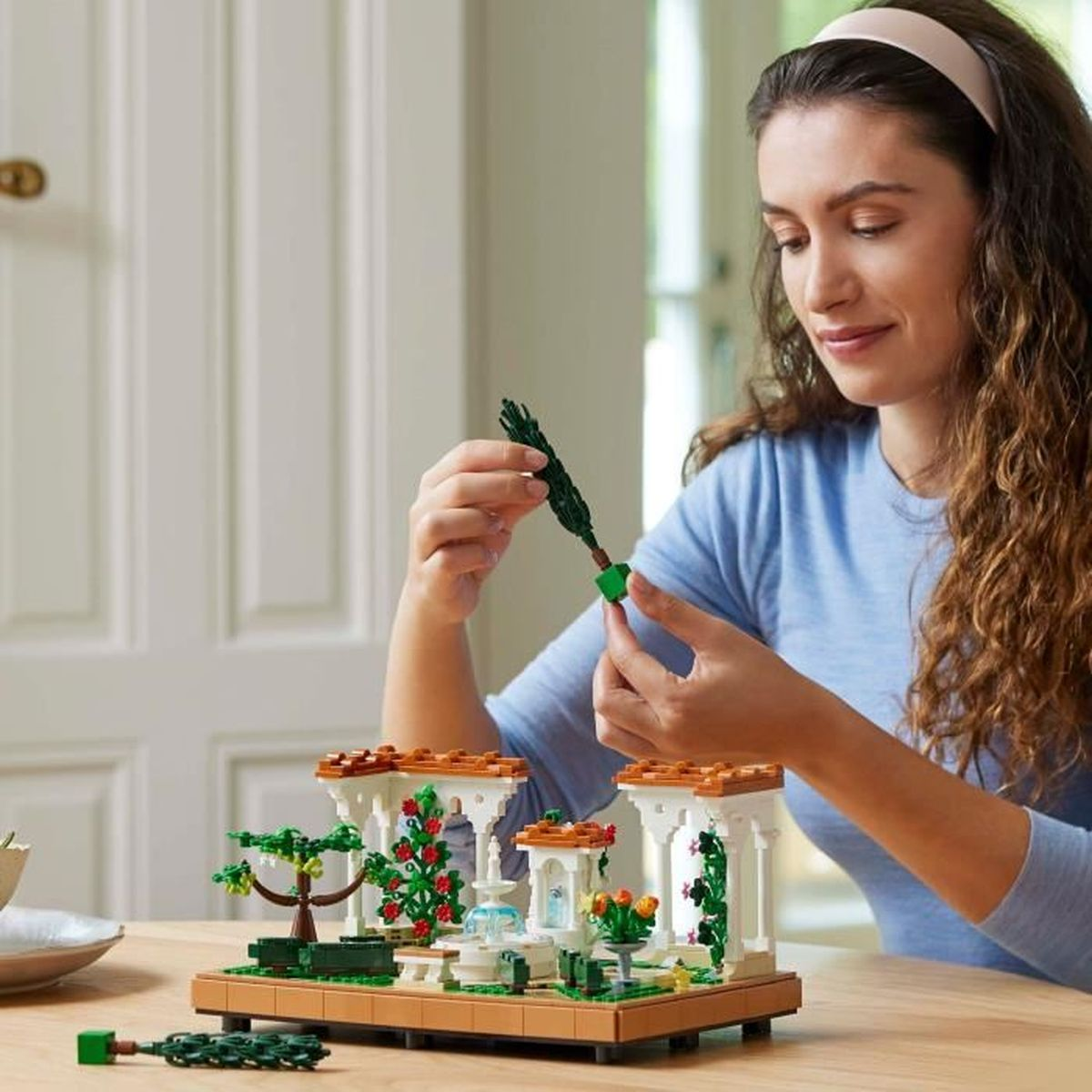 Vrouw bouwt een Lego-tuin met rozen, bomen en een fontein.