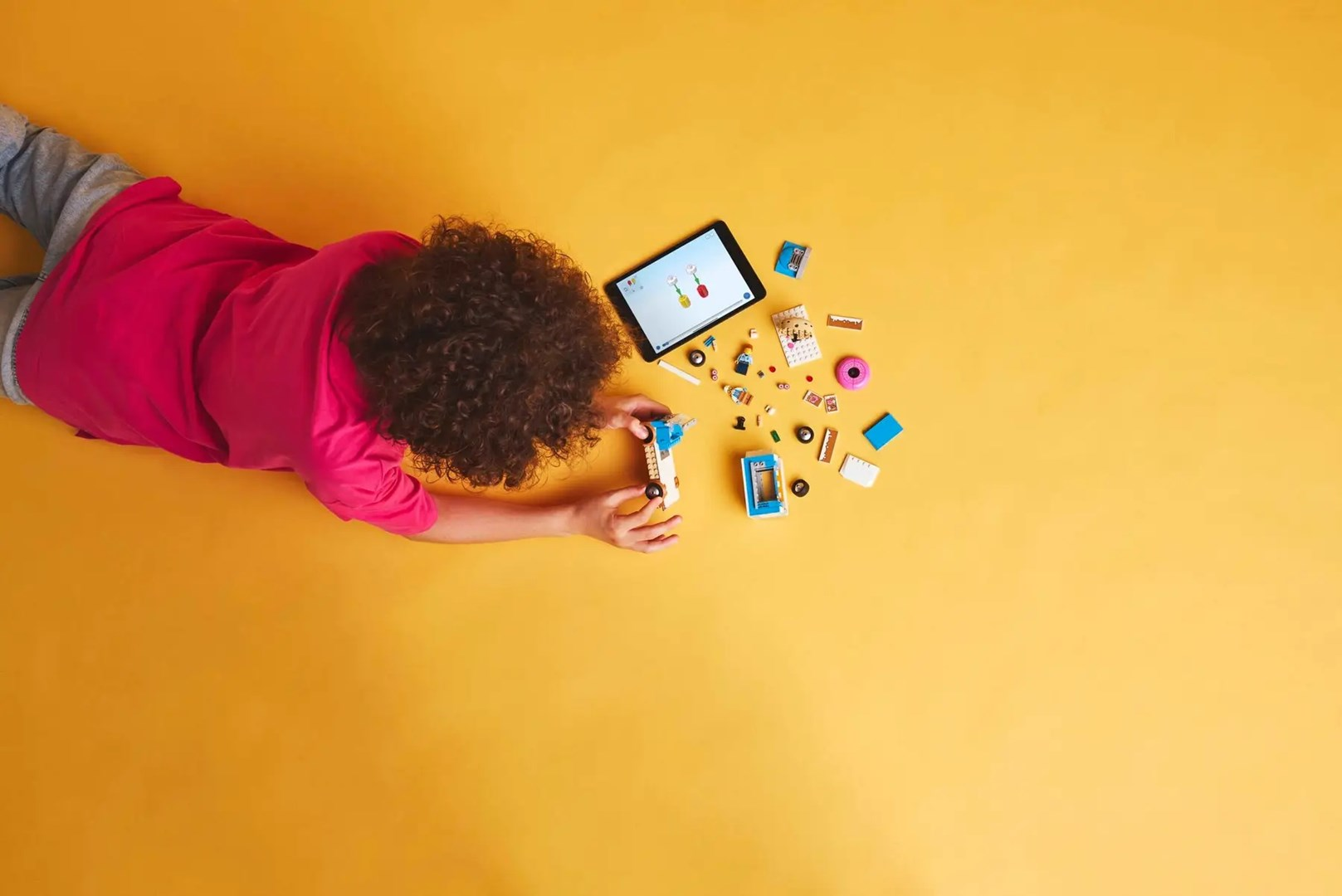 Dziecko bawi się kolorowymi klockami Lego i tabletem na żółtym tle.