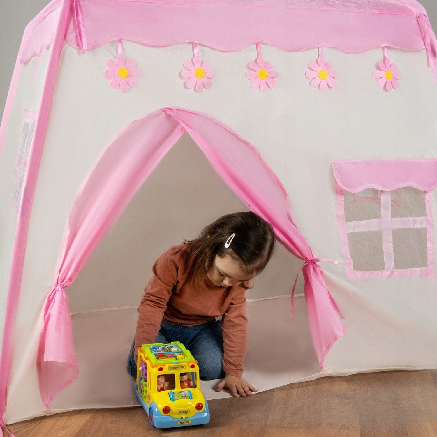 Una niña juega con un autobús de juguete dentro de una carpa rosa y blanca.