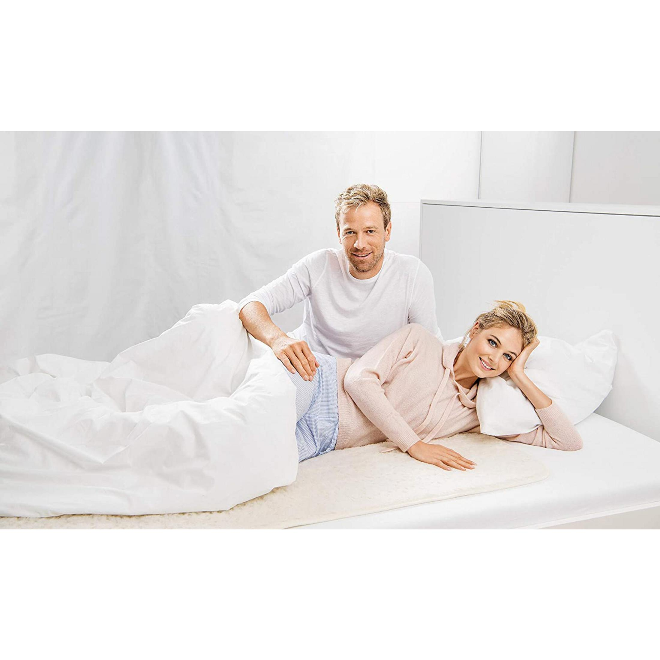 Uomo e donna sdraiati a letto su biancheria da letto bianca e tappeto color crema.