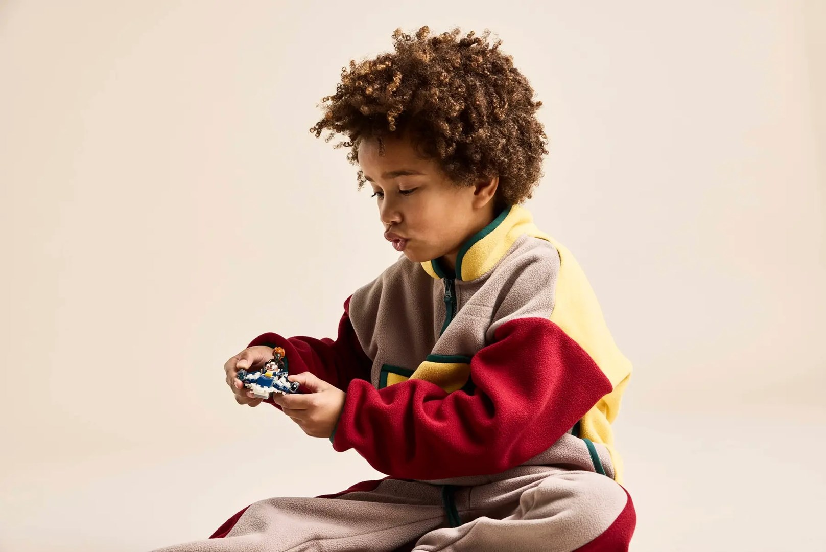 Chłopiec z kręconymi włosami trzyma w dłoniach mały niebiesko-biały samochodzik.