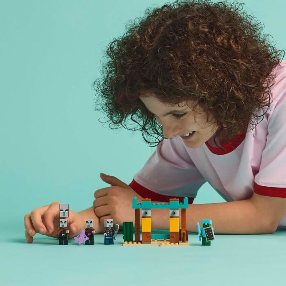 Een persoon speelt met Lego-figuren en een kleine structuur op blauwe achtergrond.