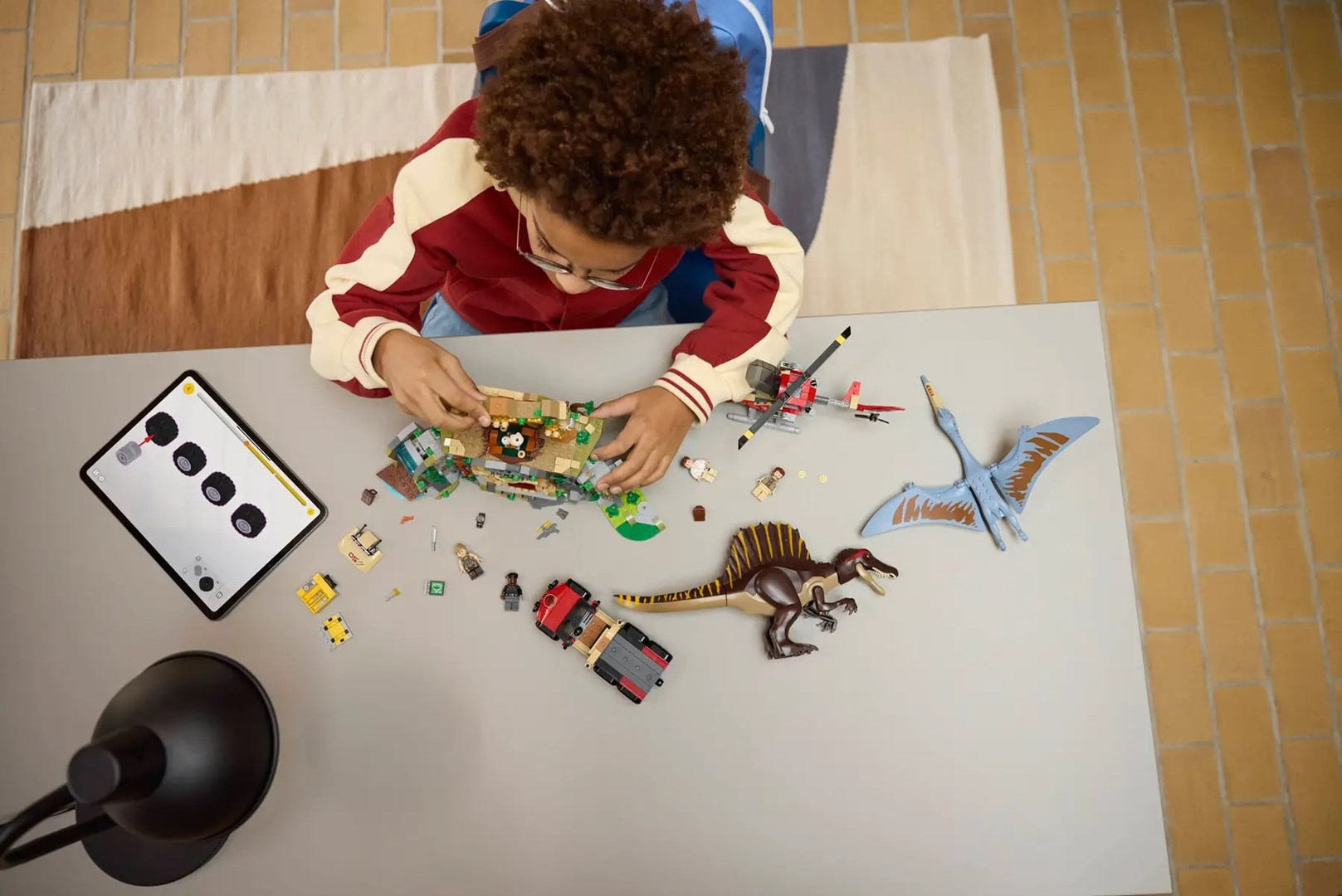 Chłopiec buduje zestaw Lego z dinozaurami i pojazdami, korzystając z tabletu.