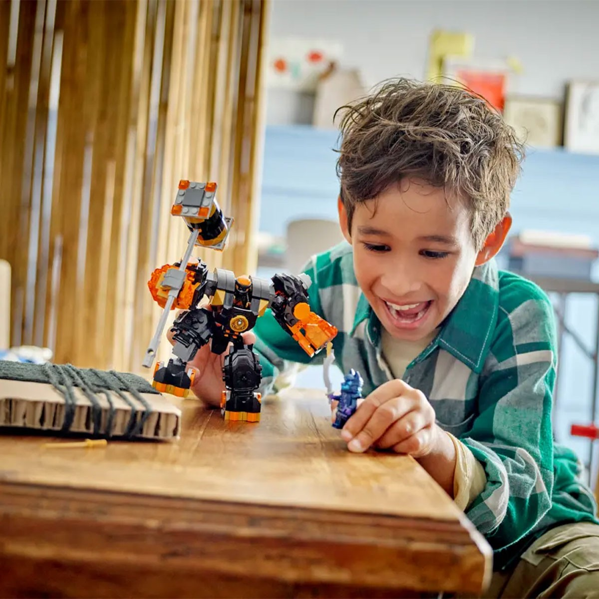 Ein Junge spielt mit einem schwarzen und orangen Roboter auf einem Holztisch.