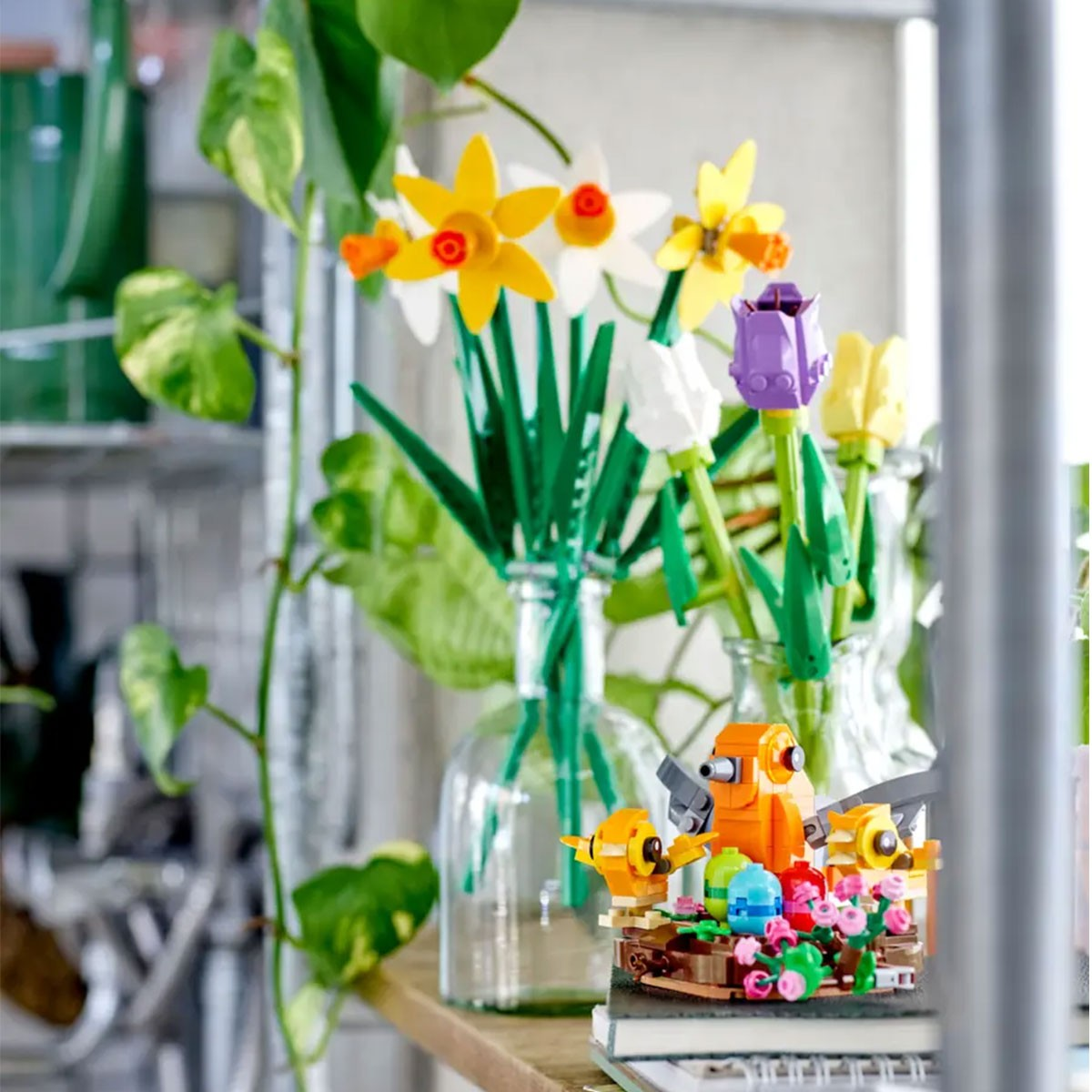 LEGO-Blumen und Vögel auf einem Regal. Weiße und gelbe Narzissen, lila und gelbe Tulpen.