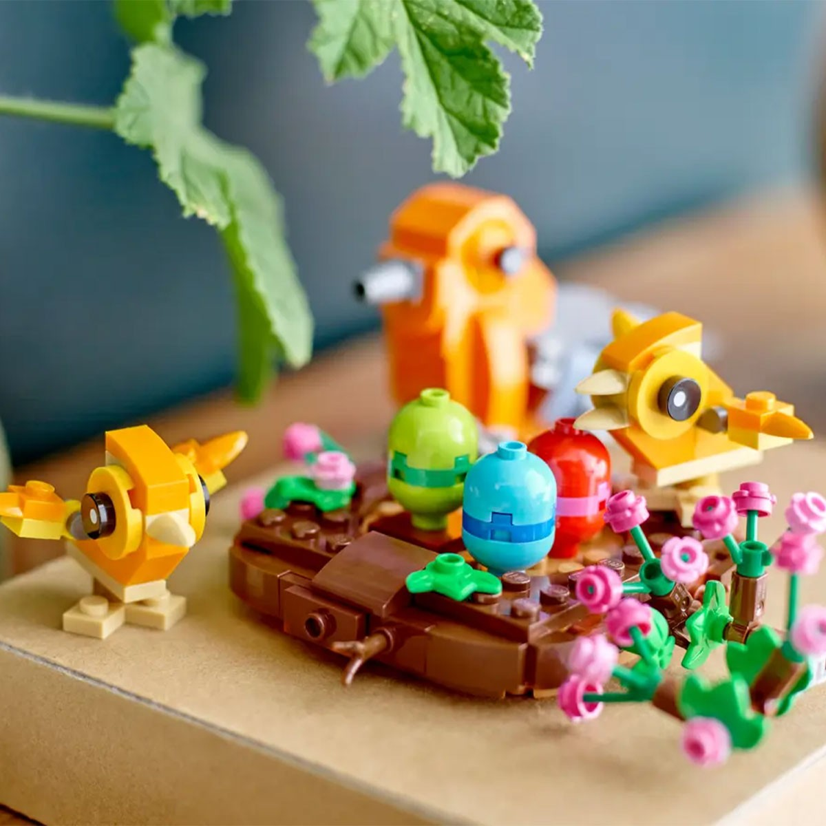 Orange Lego-Vögel mit bunten Eiern und Blumen auf brauner Basis.