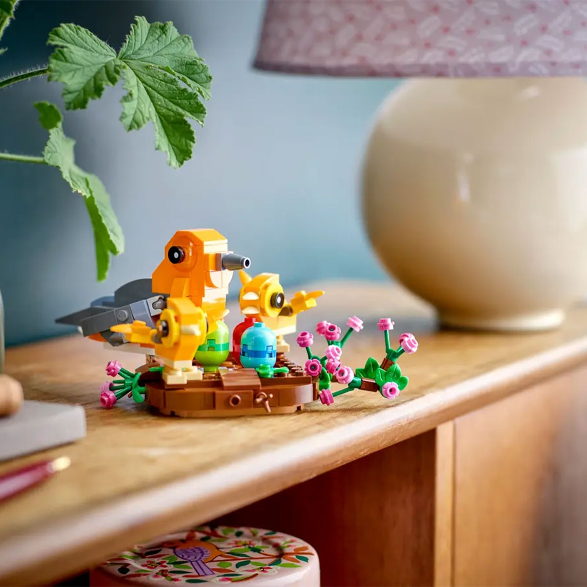 Bunte Lego-Vogelpuppen mit Küken auf einem braunen Sockel mit Blumen.